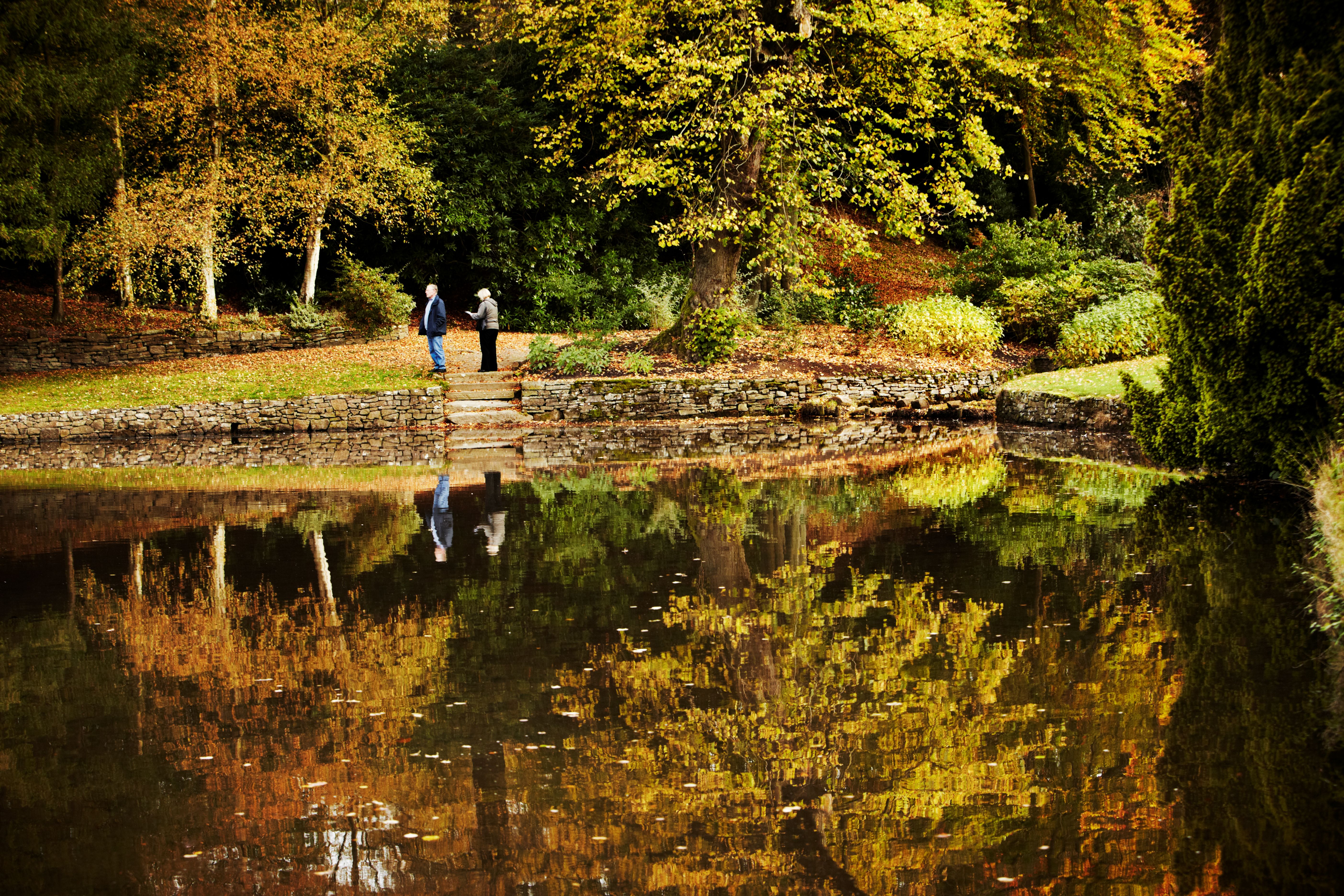 Visitors by the lake in the garden in autumn at Lyme Park, Cheshire