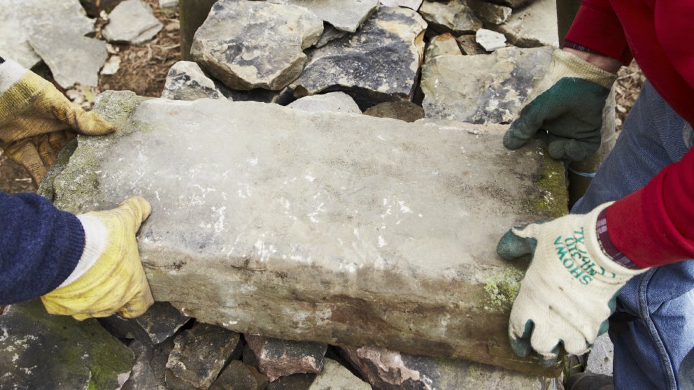 Two volunteers lifting a large stone onto a dry stone wall