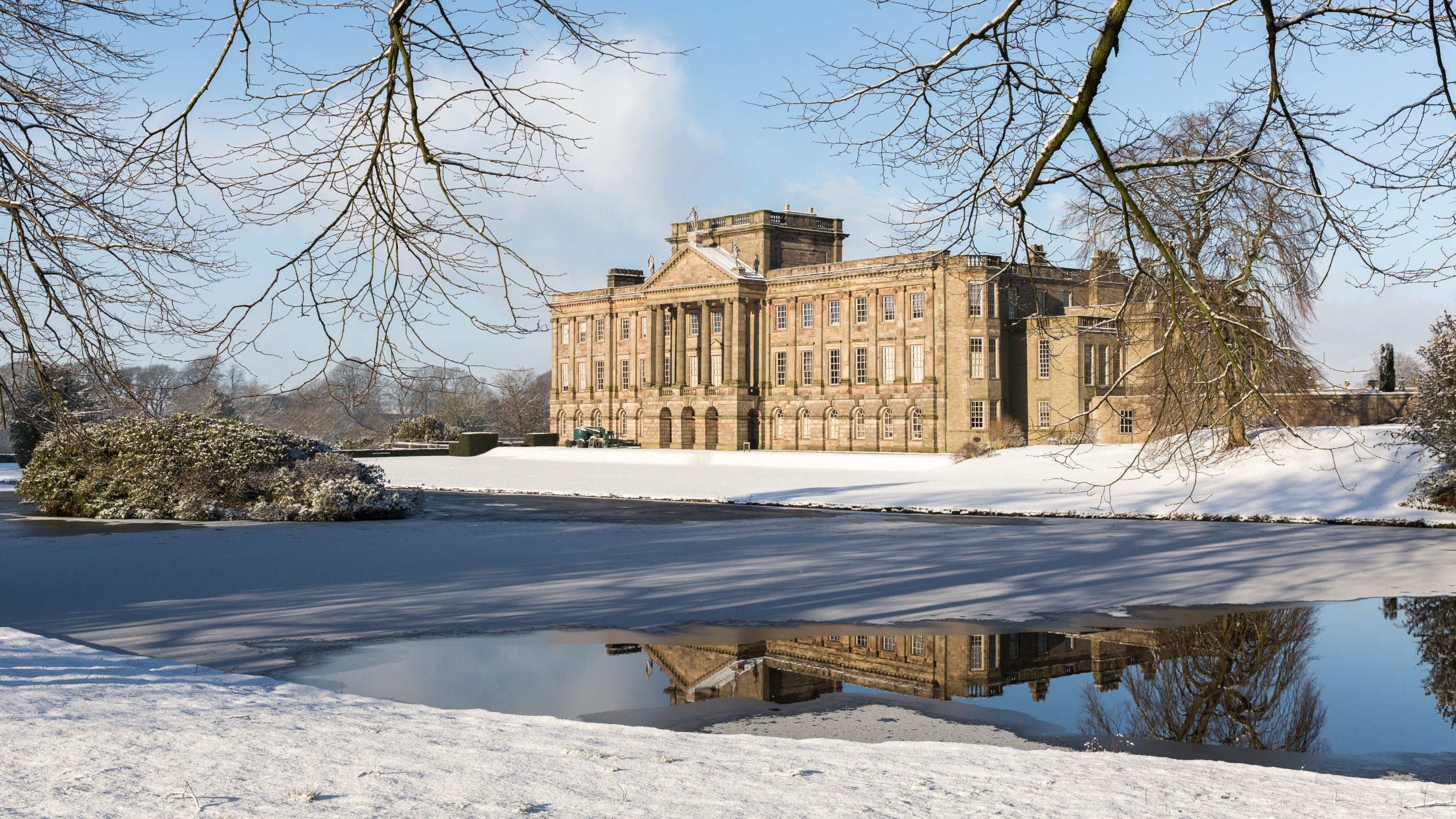 A view of Lyme house covered in snow. The house can be seen in the frozen reflection pond.