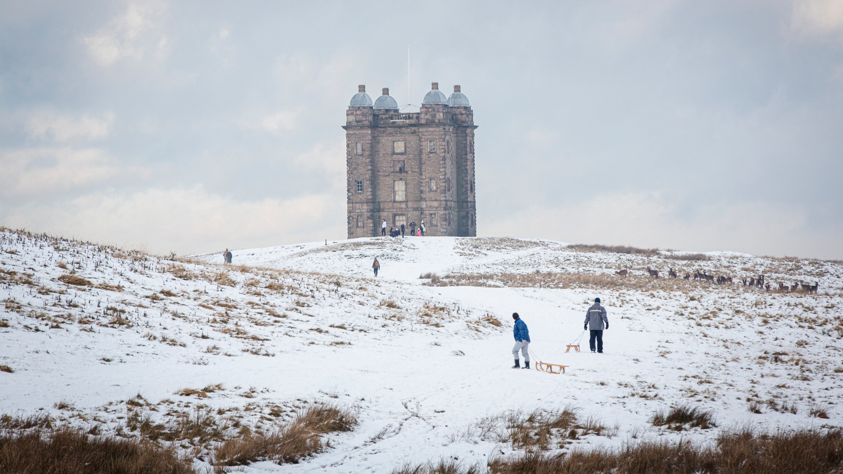 A building on a hill covered in snow. People are walking up the path to see the building.