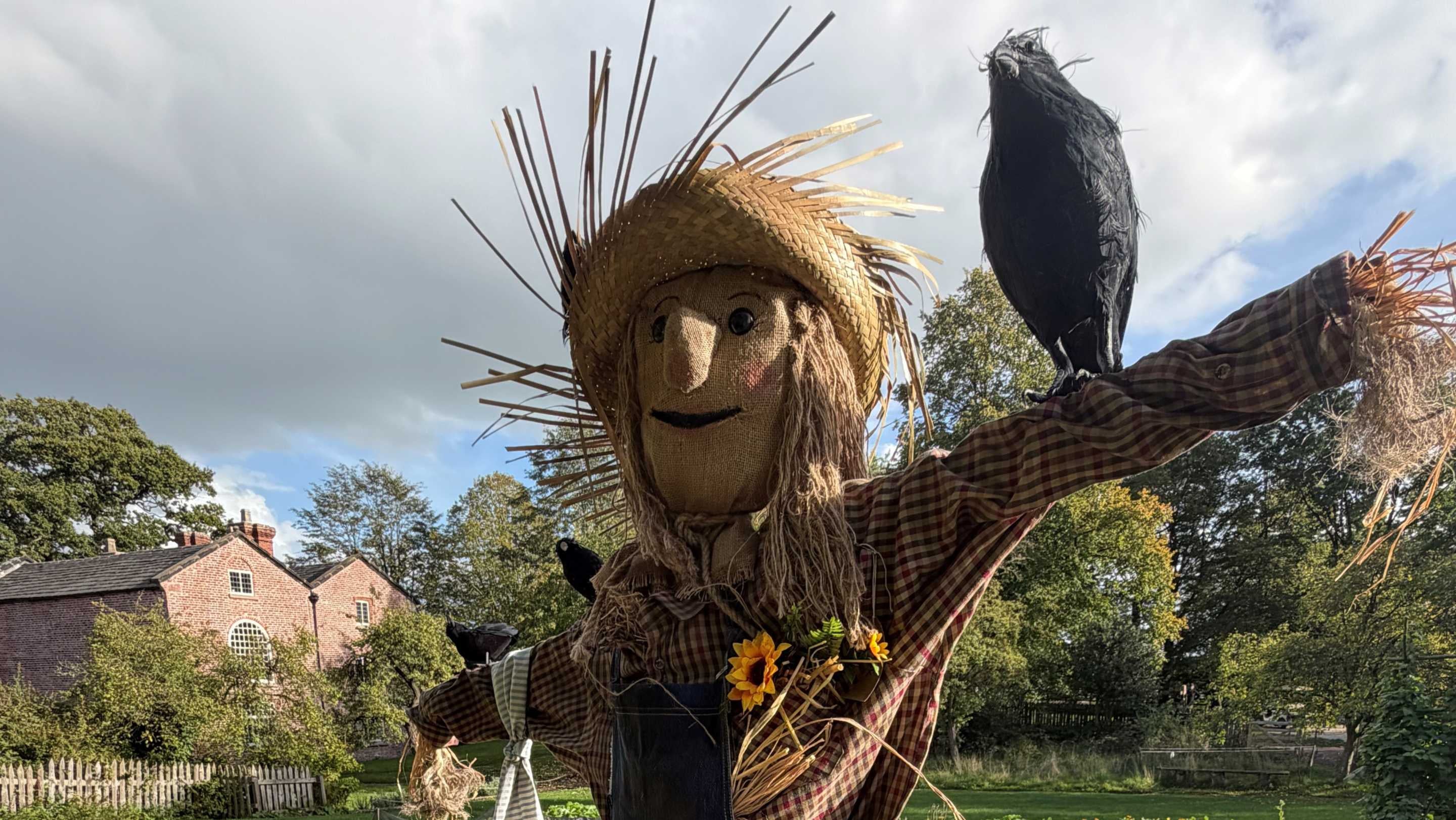 A happy scarecrow with a red brick building in the background