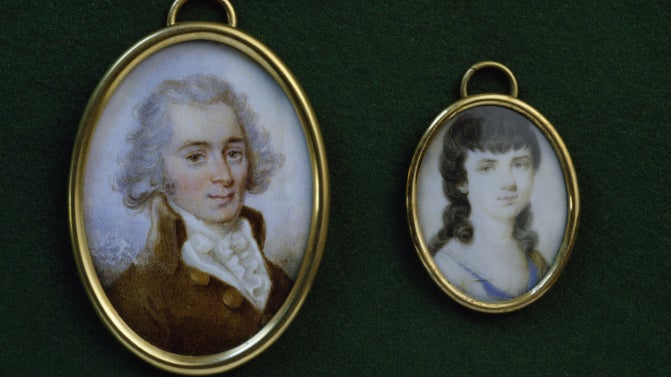 Gold oval frames holding paintings. One of a grey haired haired man, and the other a young women with long brown curlt hair. Both in period dress.