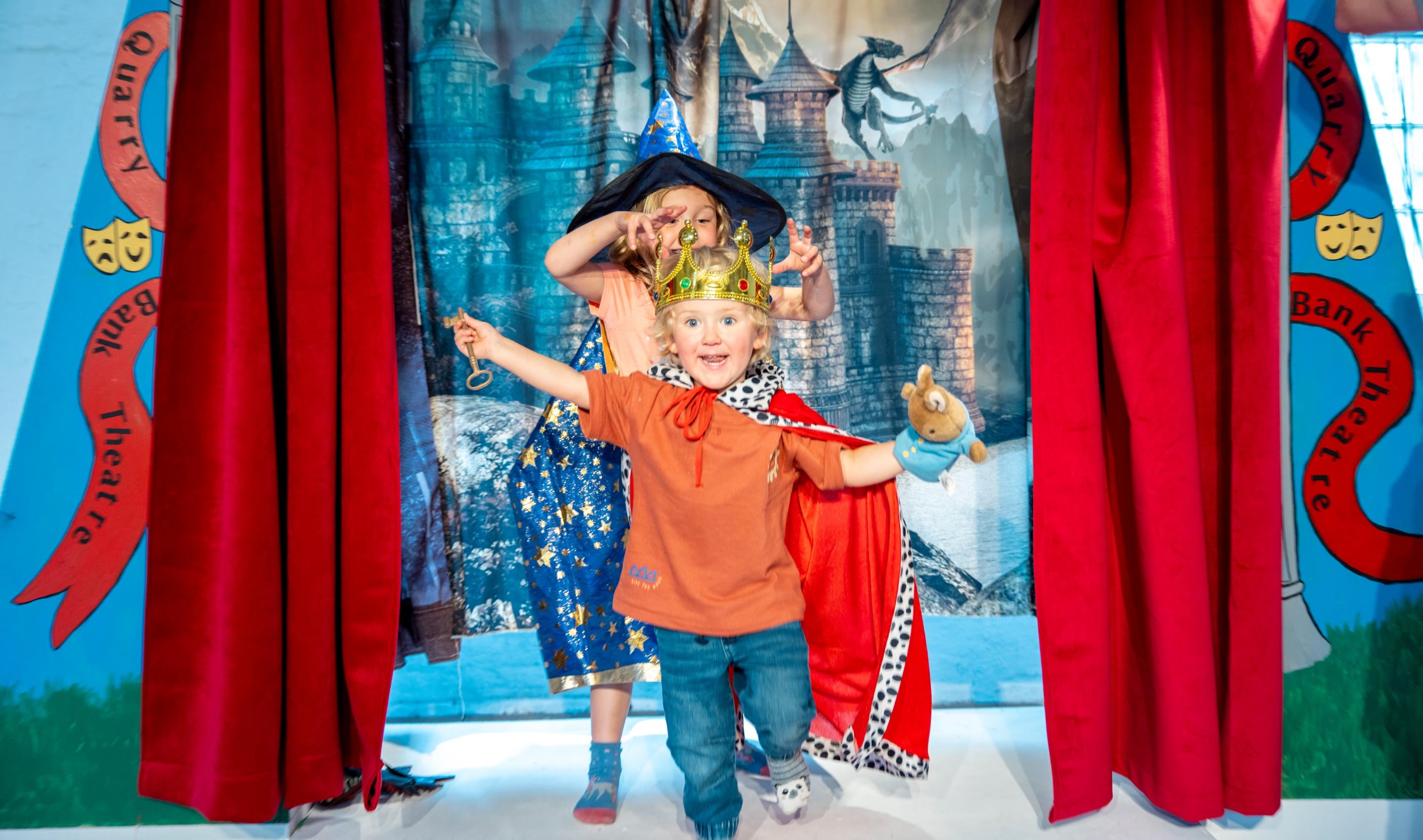 Two children walking through a red curtain on a play stage