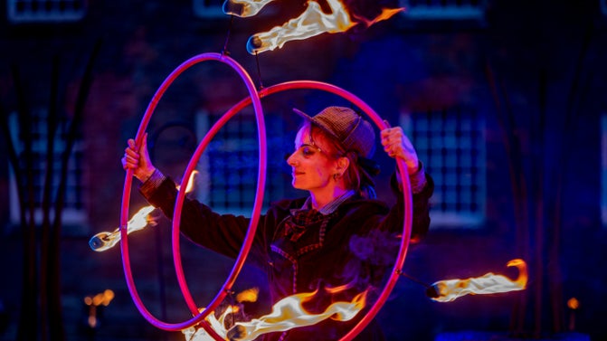 Lady wearing a hat holdig two rings which are on fire.