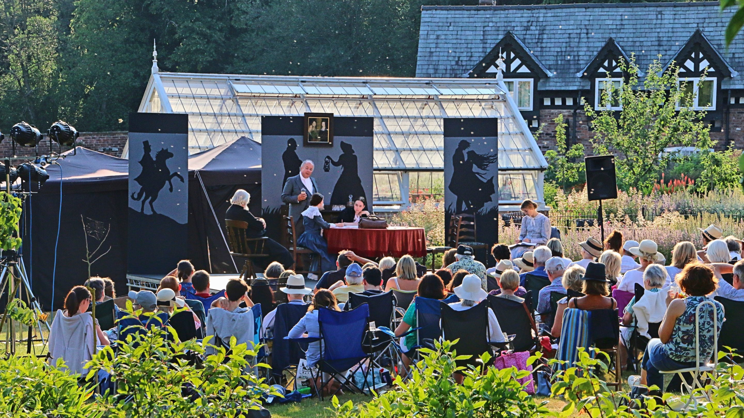 A group of people sat on the grass looking at a stage with actors performing