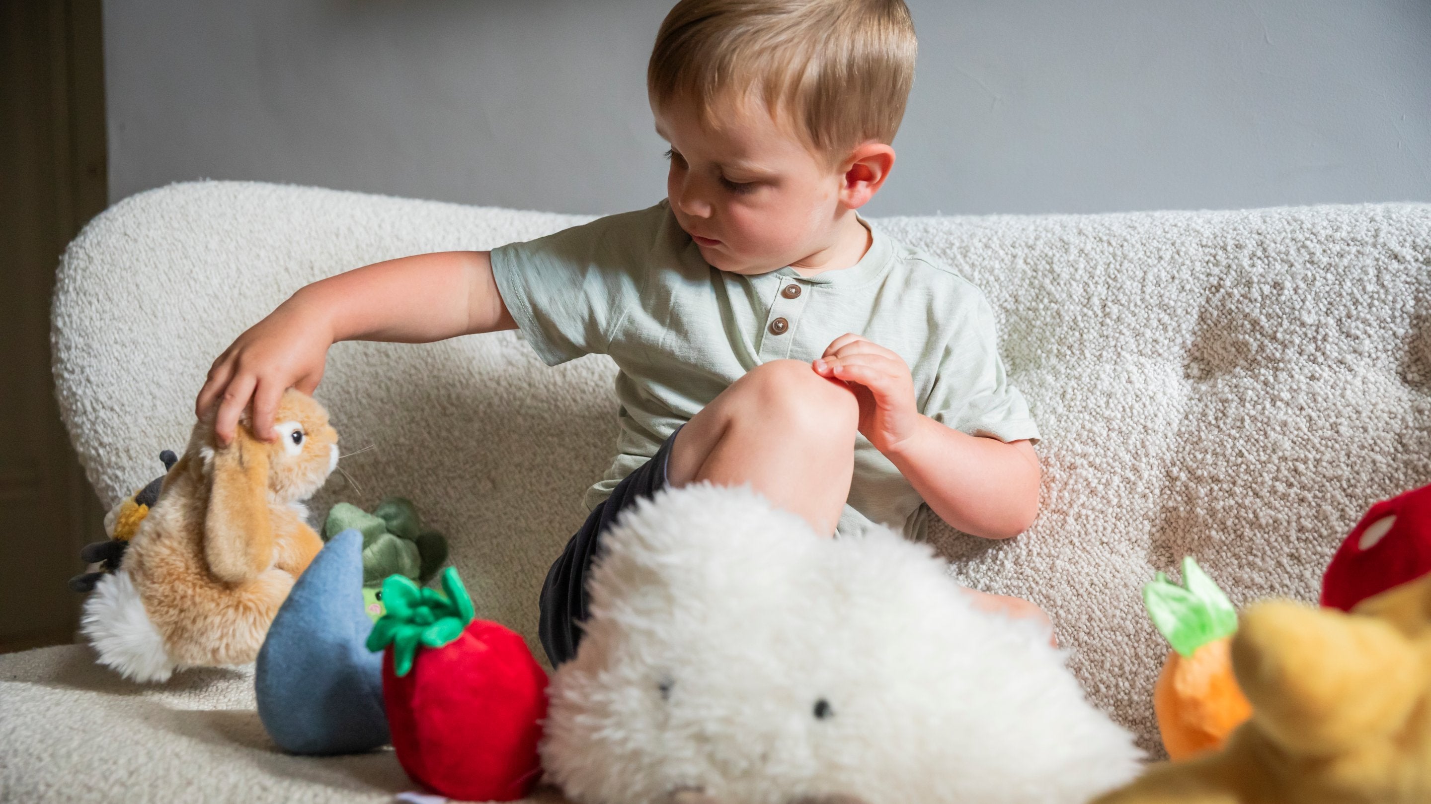 A toddler sat on a sifa playing with soft toys