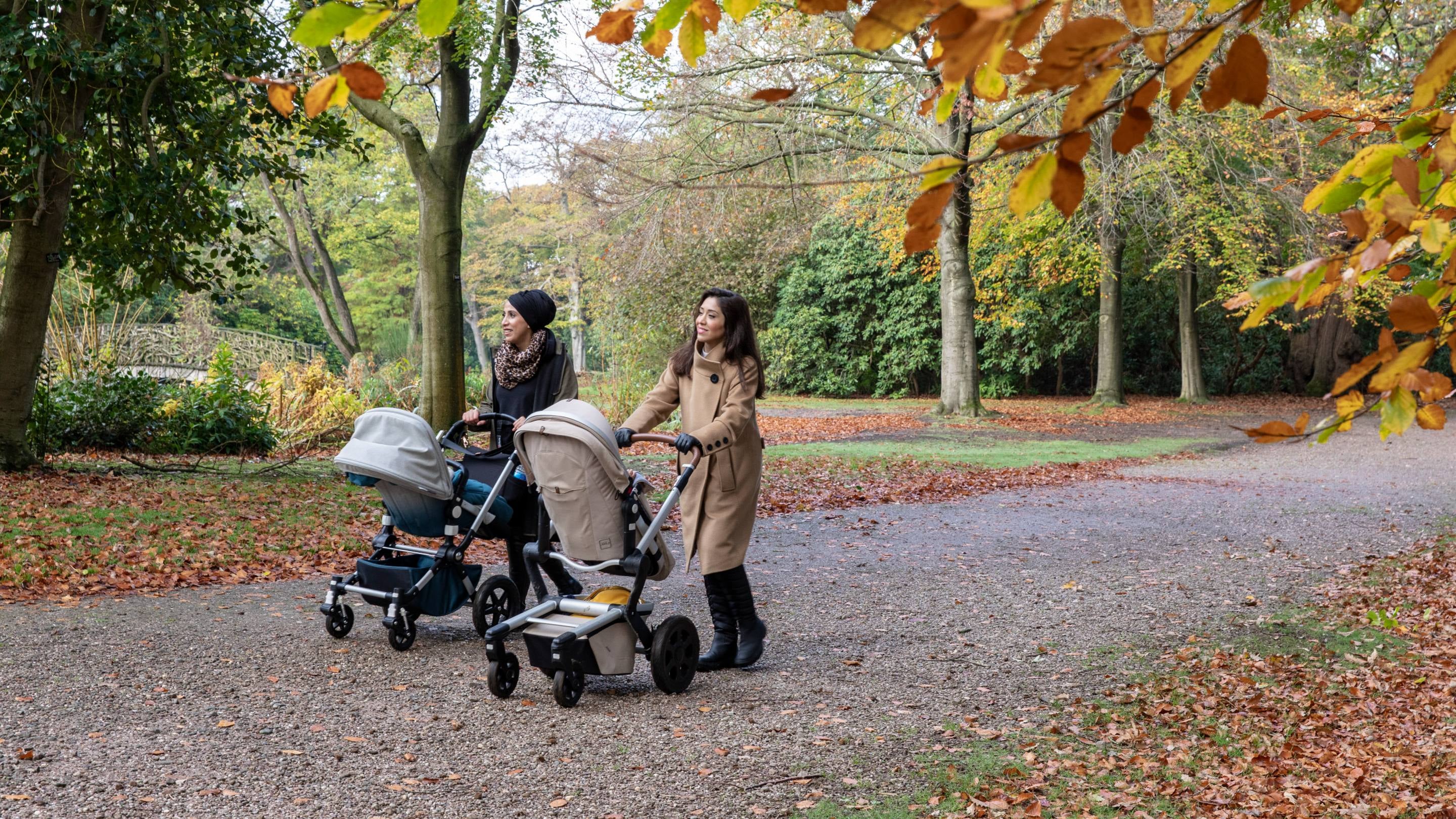 Two visitors walking with their push chairs through the Japanese Gardens in autumn at Tatton Park, Cheshire, with leaves on the floor all around them.