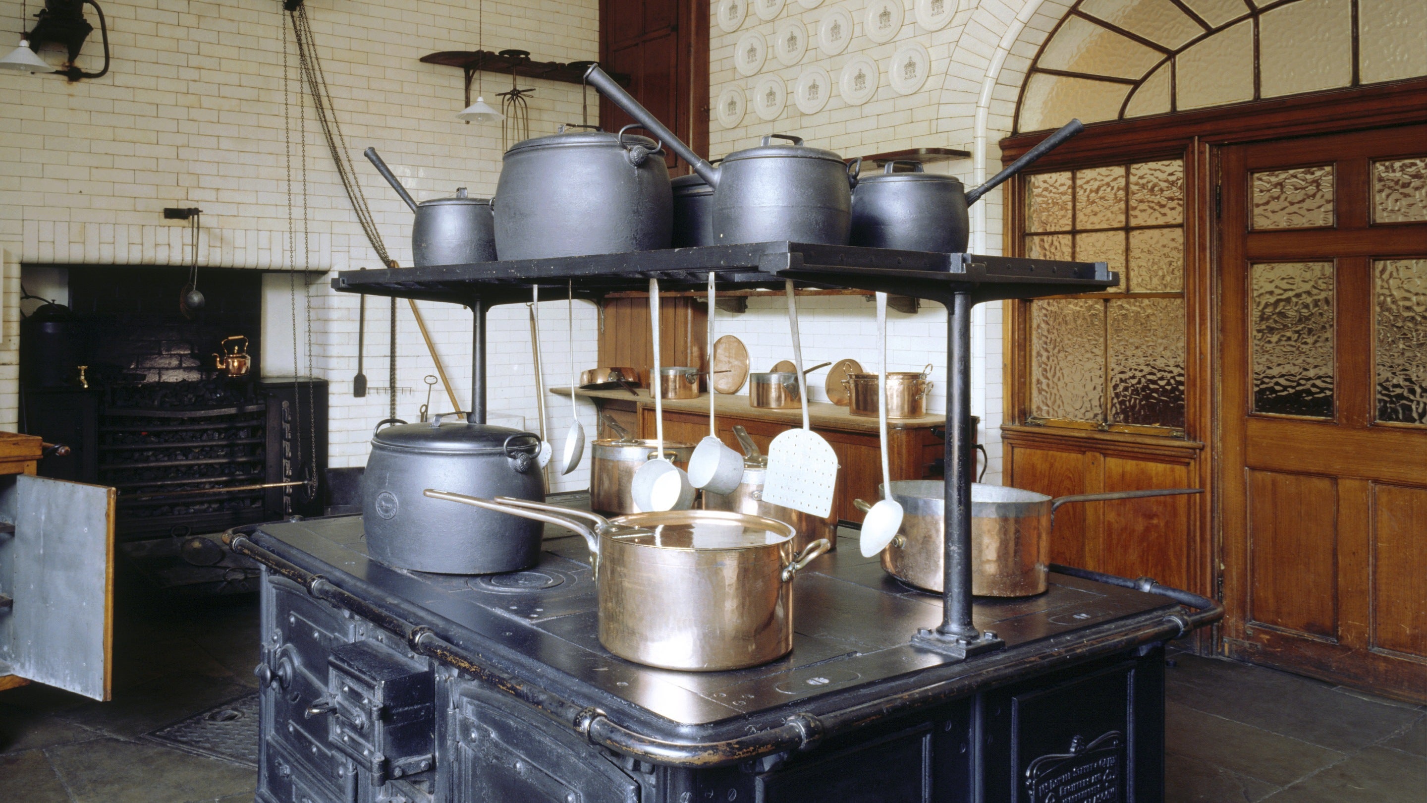 Inside the Kitchen at Tatton Park, Cheshire, where a black wrought-iron range stands in the middle of the stone floor, covered with pots, pans and utensils.