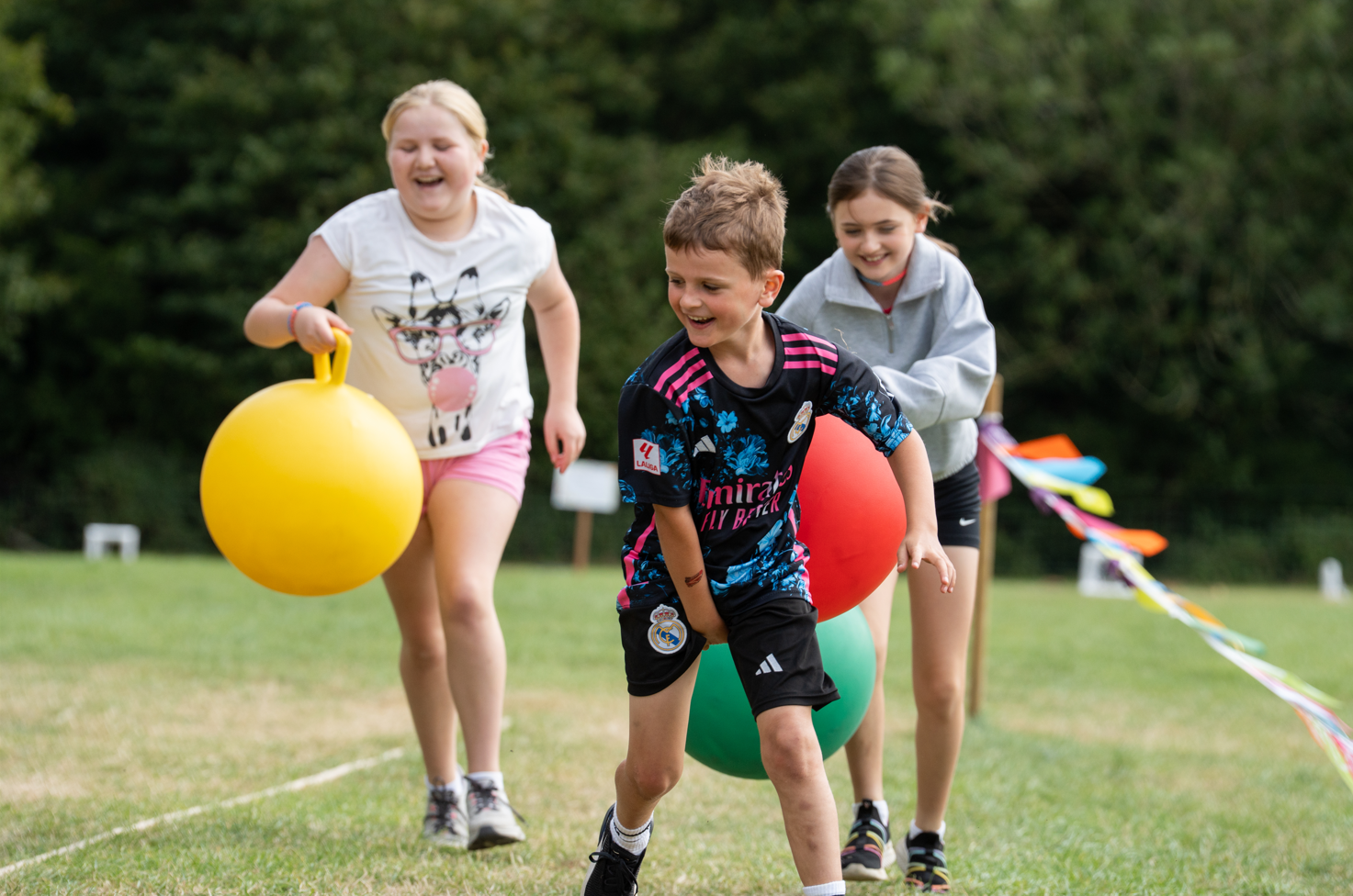 Three children play a running race holding space hoppers.