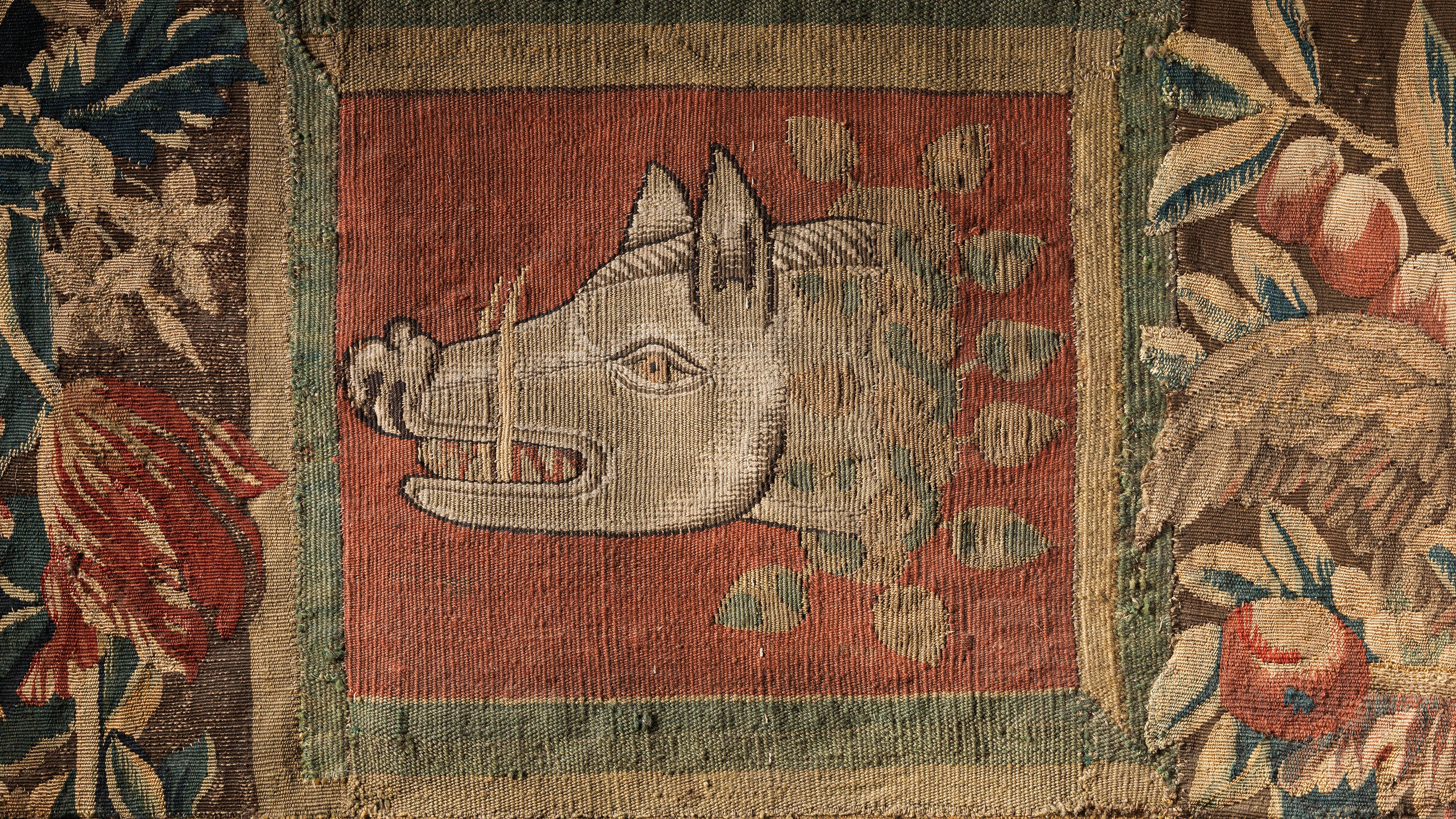 Detail of a tapestry showing a boar's head facing left with garlands of flowers to the left and right