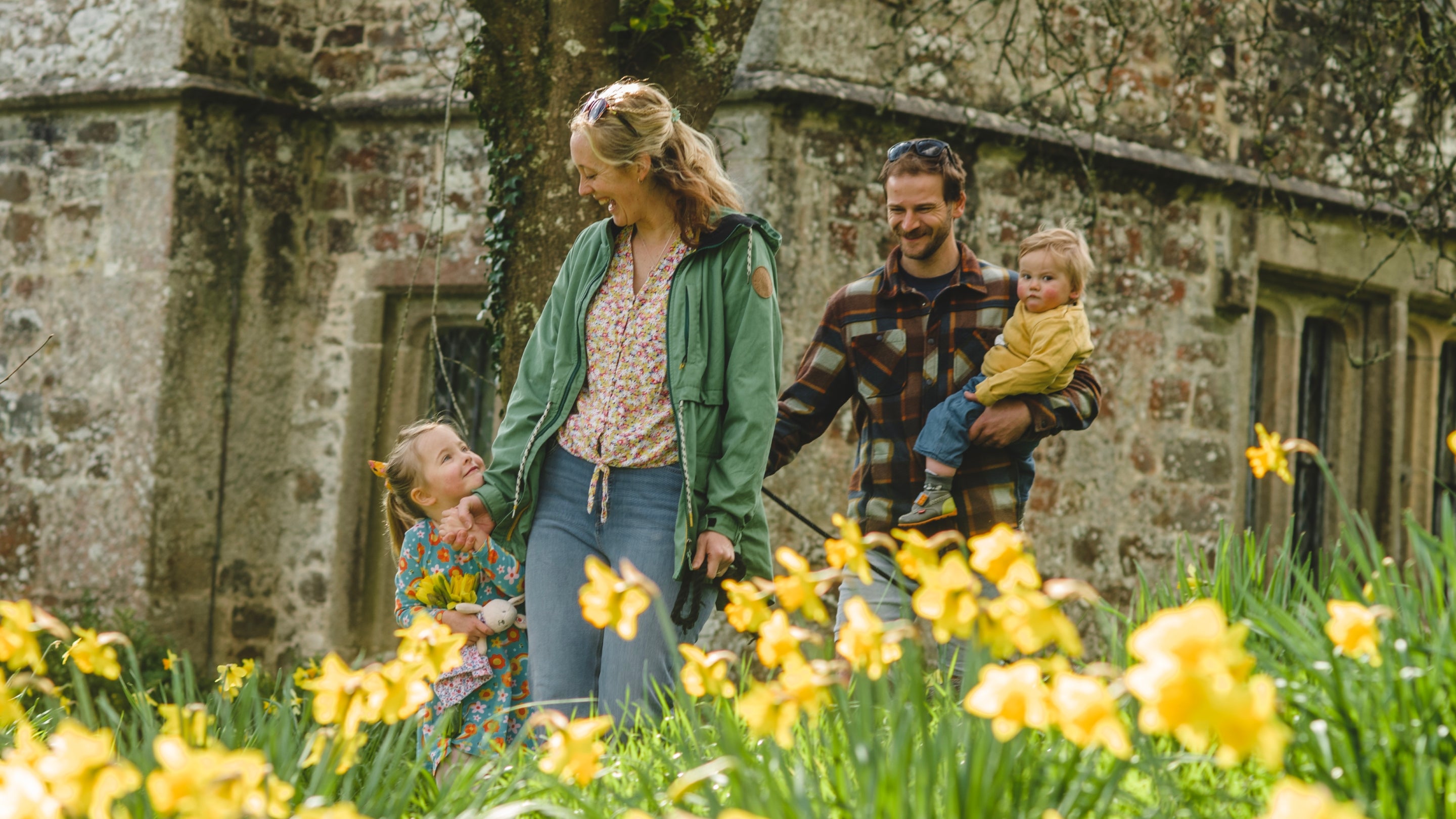 A family walking together in daffodils at Cotehele smiling wearing colourful clothes.