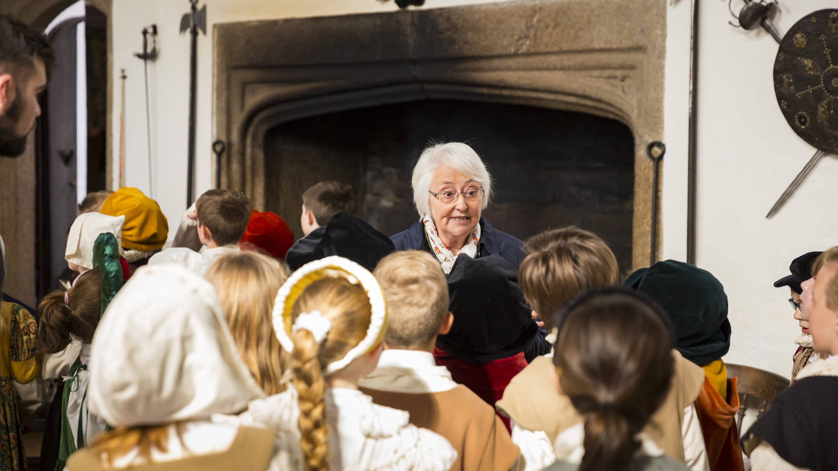A volunteer room guide talks to a group of school children dressed in Tudor clothes inside the Great Hall at Cotehele, Cornwall