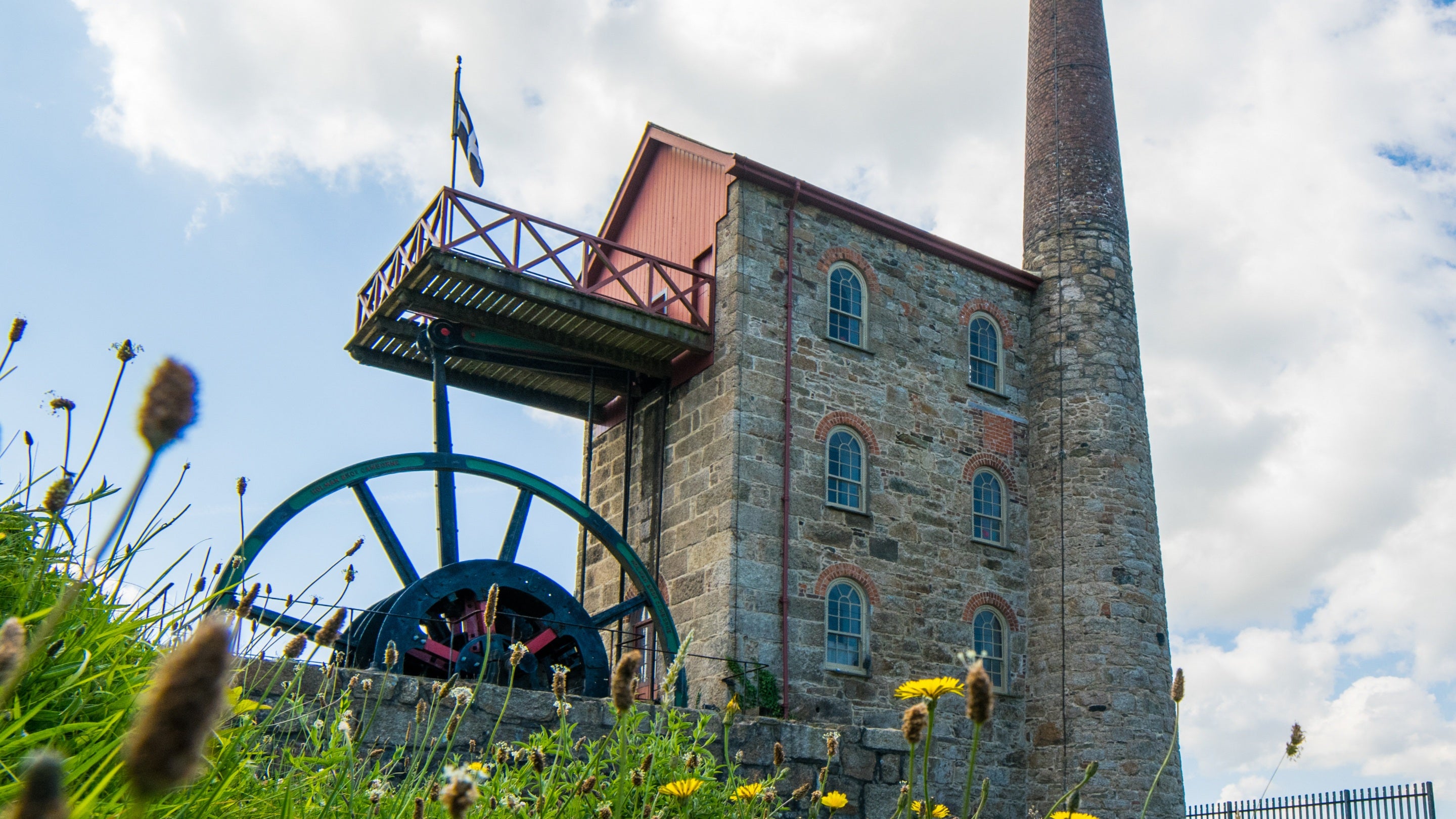 The exterior of Michell's Engine House at East Pool Mine, Cornwall, a brick building with a tall chimney stack attached to it.