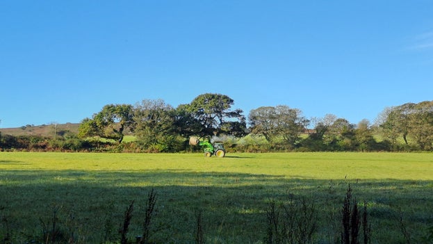 A tractor crosses a green field at Godolphin, carrying a hay bale.