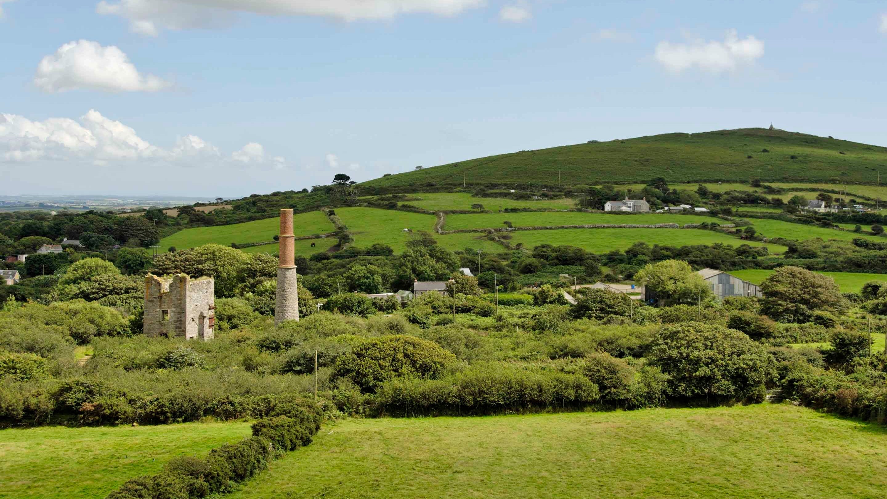 View across fields at Goldolphin House, in Cornwall, with abandoned pit head buildings in the foreground