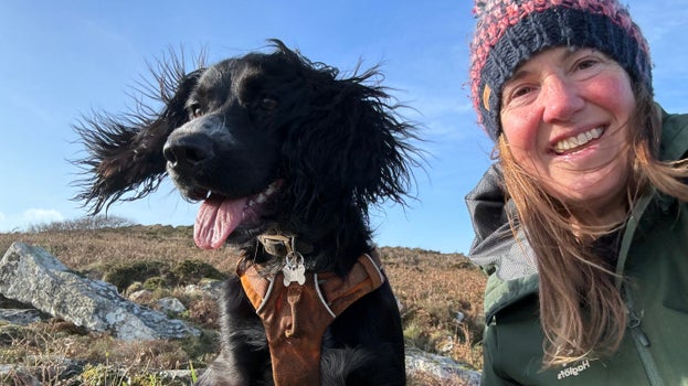 Lochy, a spaniel & her owner Vicki visiting Godolphin Hill. Lochy is wearing an orange harness & Vicki has on a woolly hat & green jacket.