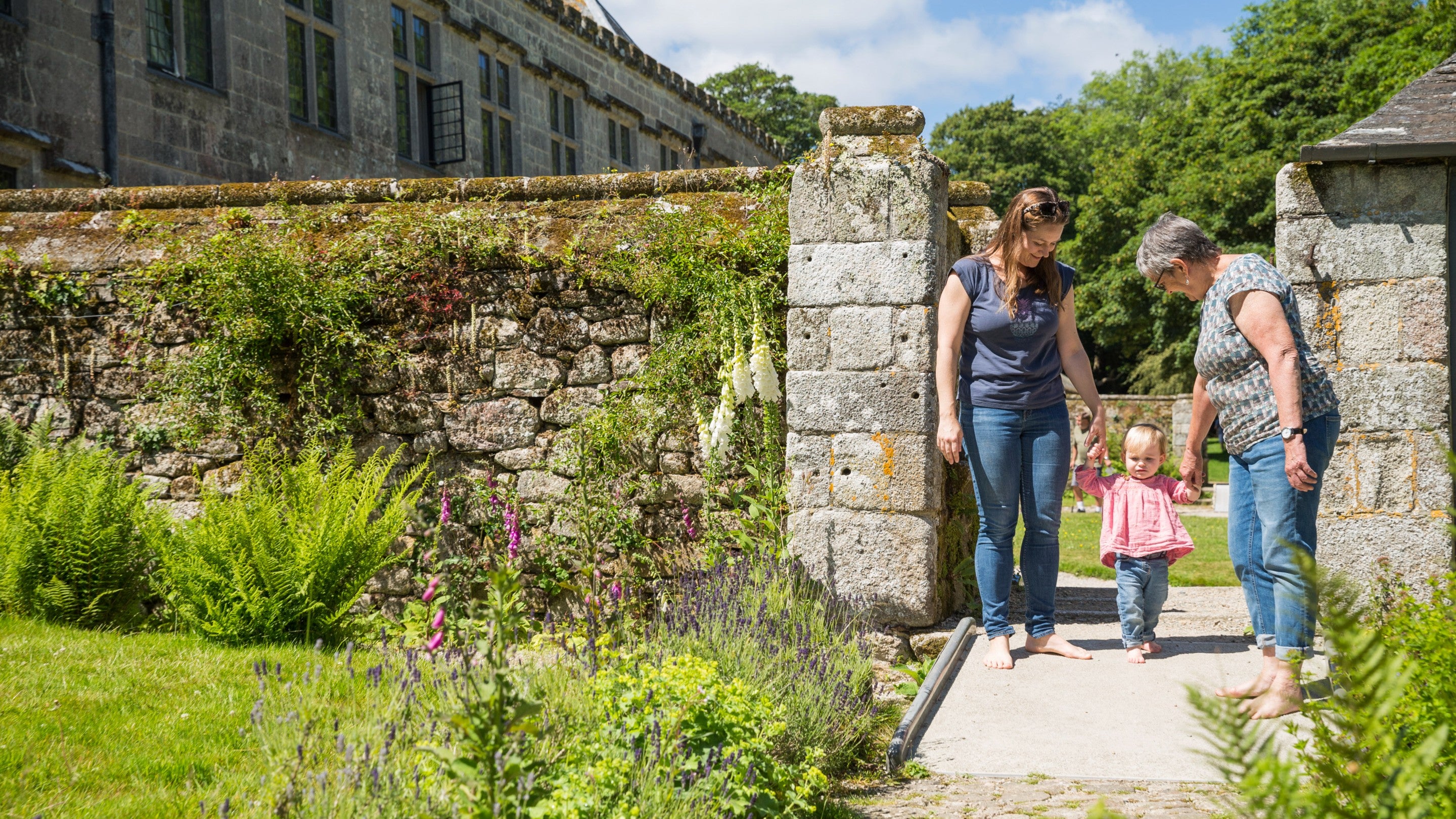 Two visitors each holding the hand of a toddler in the garden in June at Godolphin, Cornwall