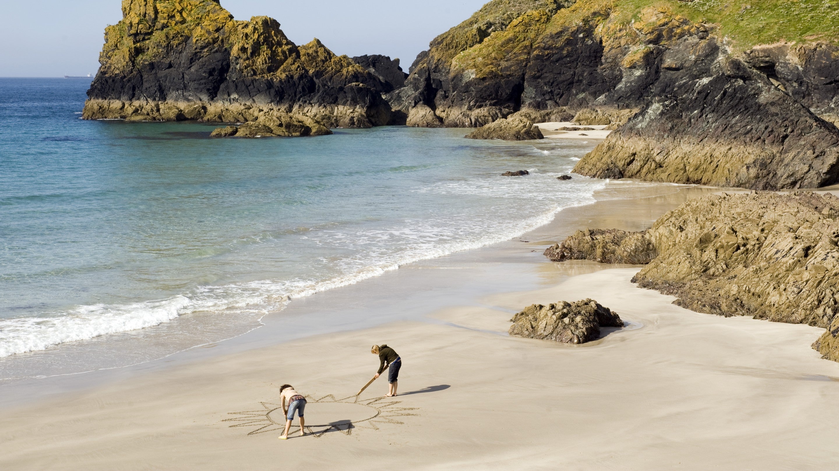 Visitors draw a huge sun on the sandy beach at Kynance Cove, Cornwall