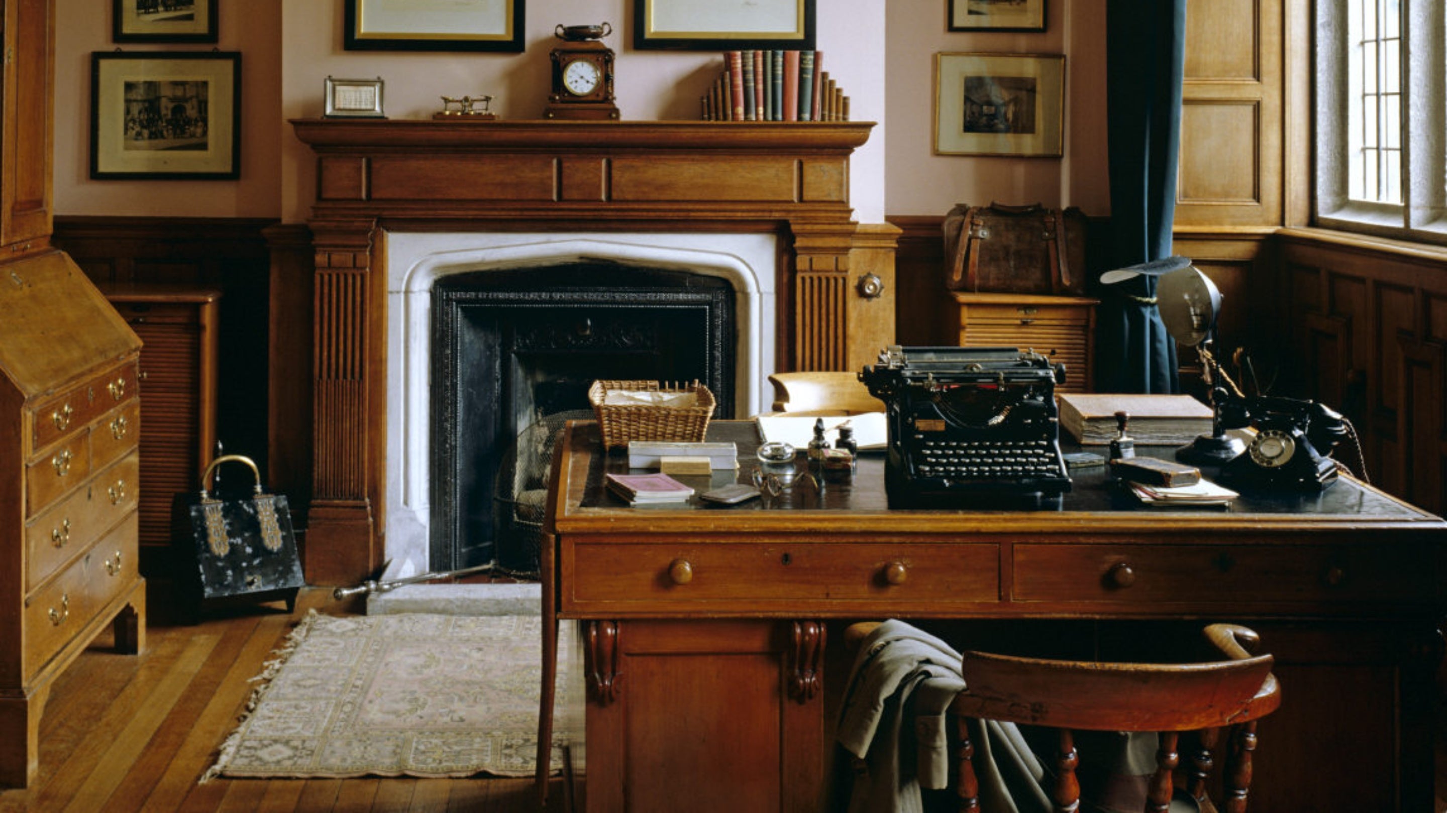 View of the Steward's Room at Lanhydrock with a pine desk with a black phone and typewriter on it, wooden chair, wooden chests of drawers and a fireplace