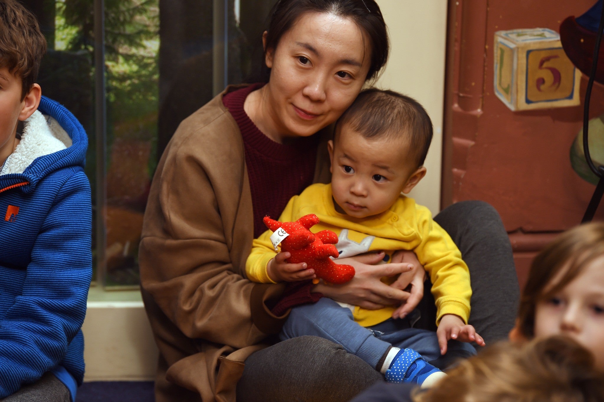 An adult holding a young child during a family activity at Lanhydrock. The child is holding a small red soft toy.