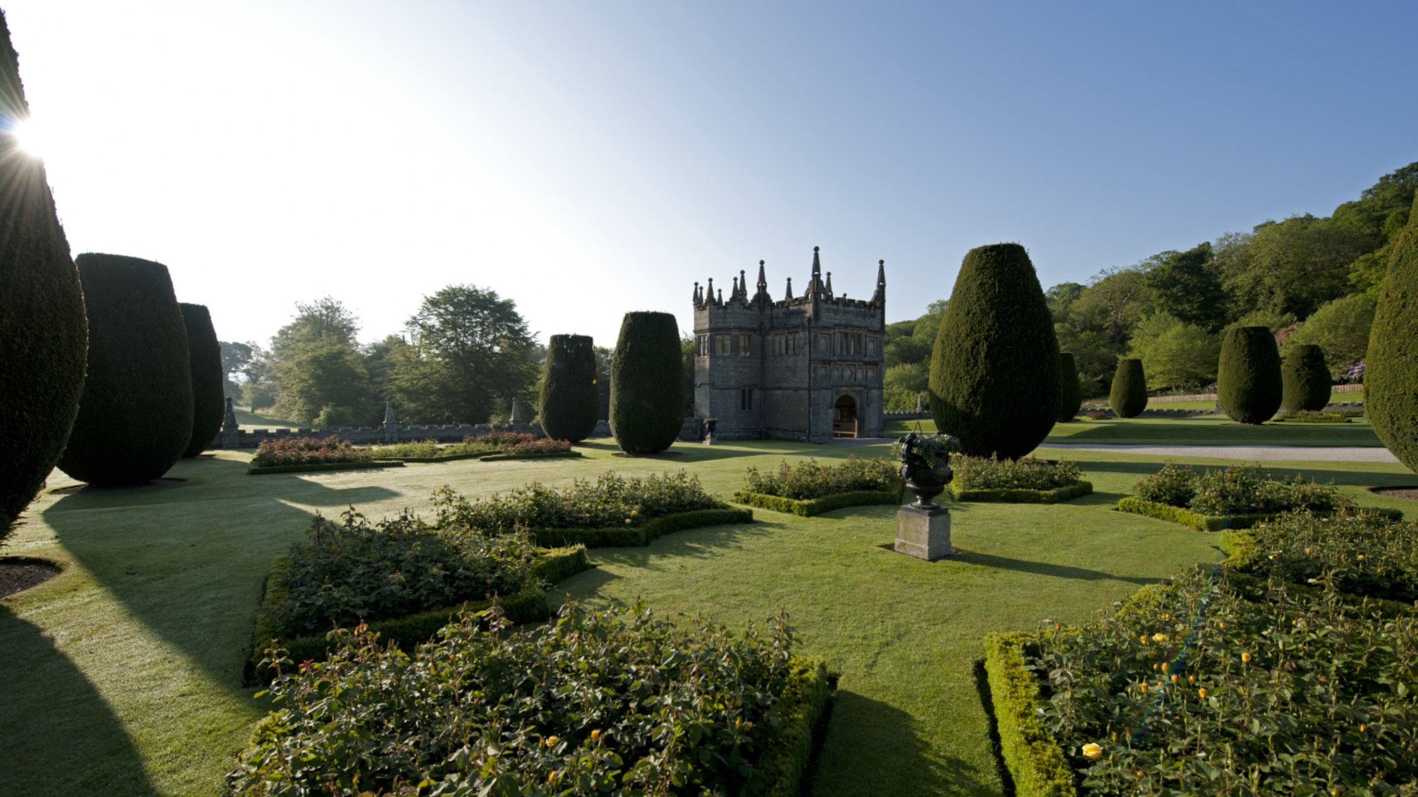 The garden looking towards the gatehouse at Lanhydrock. There are green hedges and the grey building in the background.