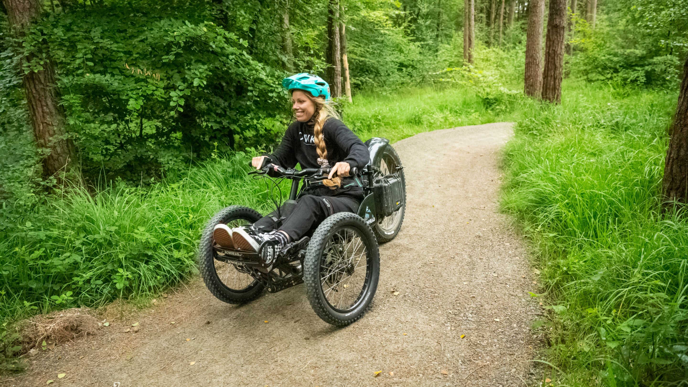 Visitor exploring the wooded cycle trails at Lanhydrock, Cornwall with long grass either side of the path and trees in the background