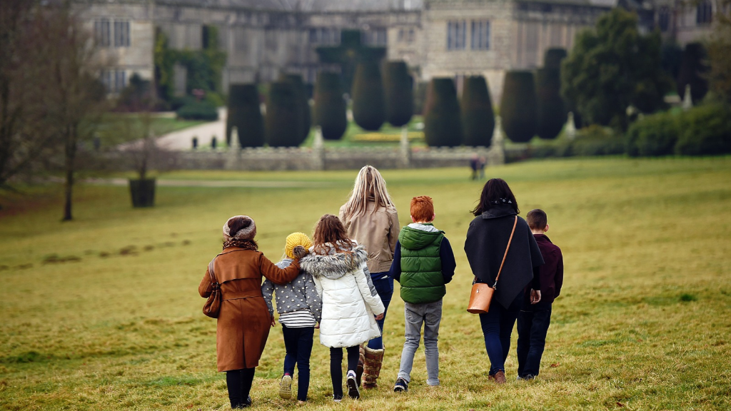 A group of adults and children walking across the parkland towards Lanhydrock house and garden.