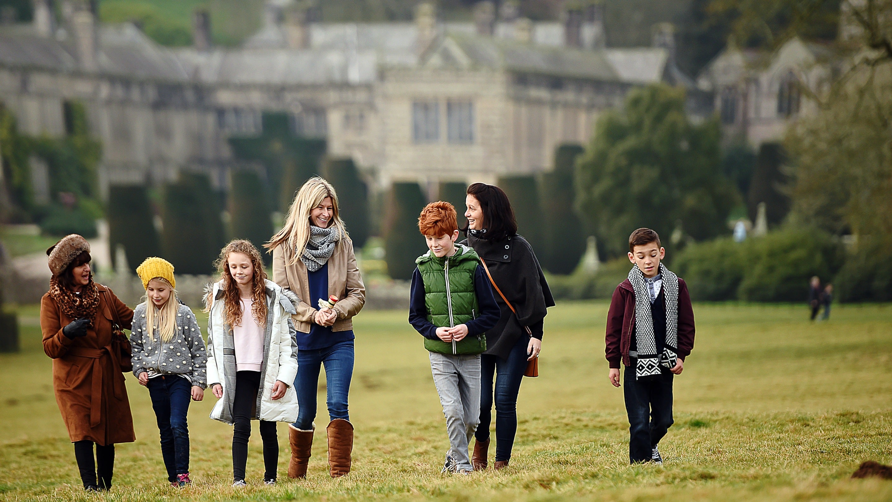 Adults and children enjoying a walk around the parkland with the house in the background at Lanhydrock, Cornwall