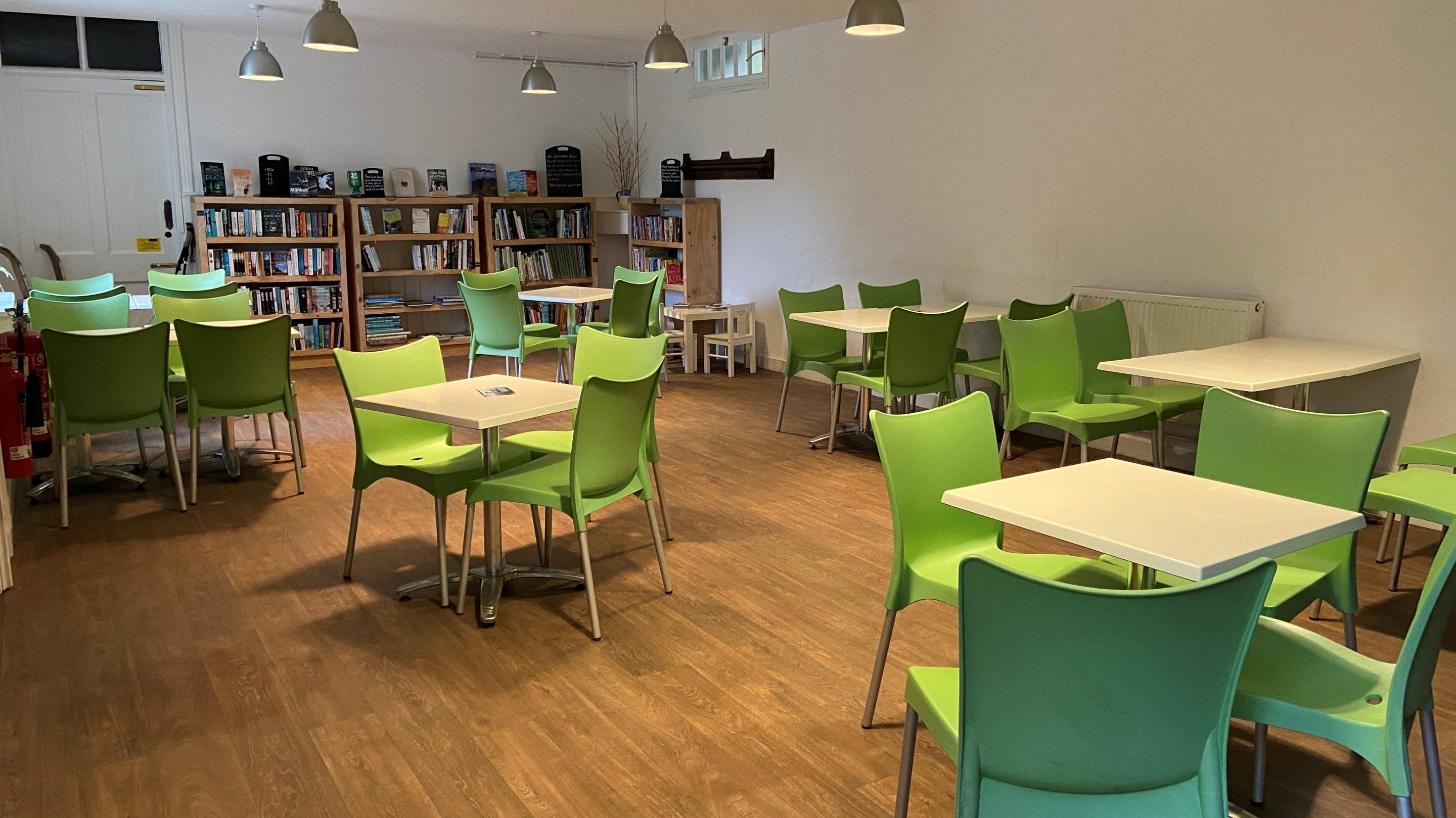 White tables & green chairs at Penrose, with second-hand bookshelves in the background.