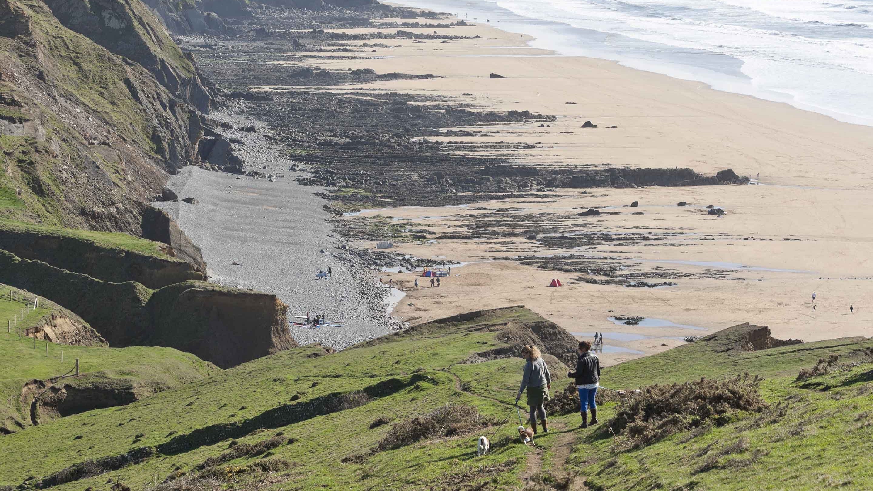 Dog walkers on the cliff top above the coast at Sandymouth, Cornwall.
