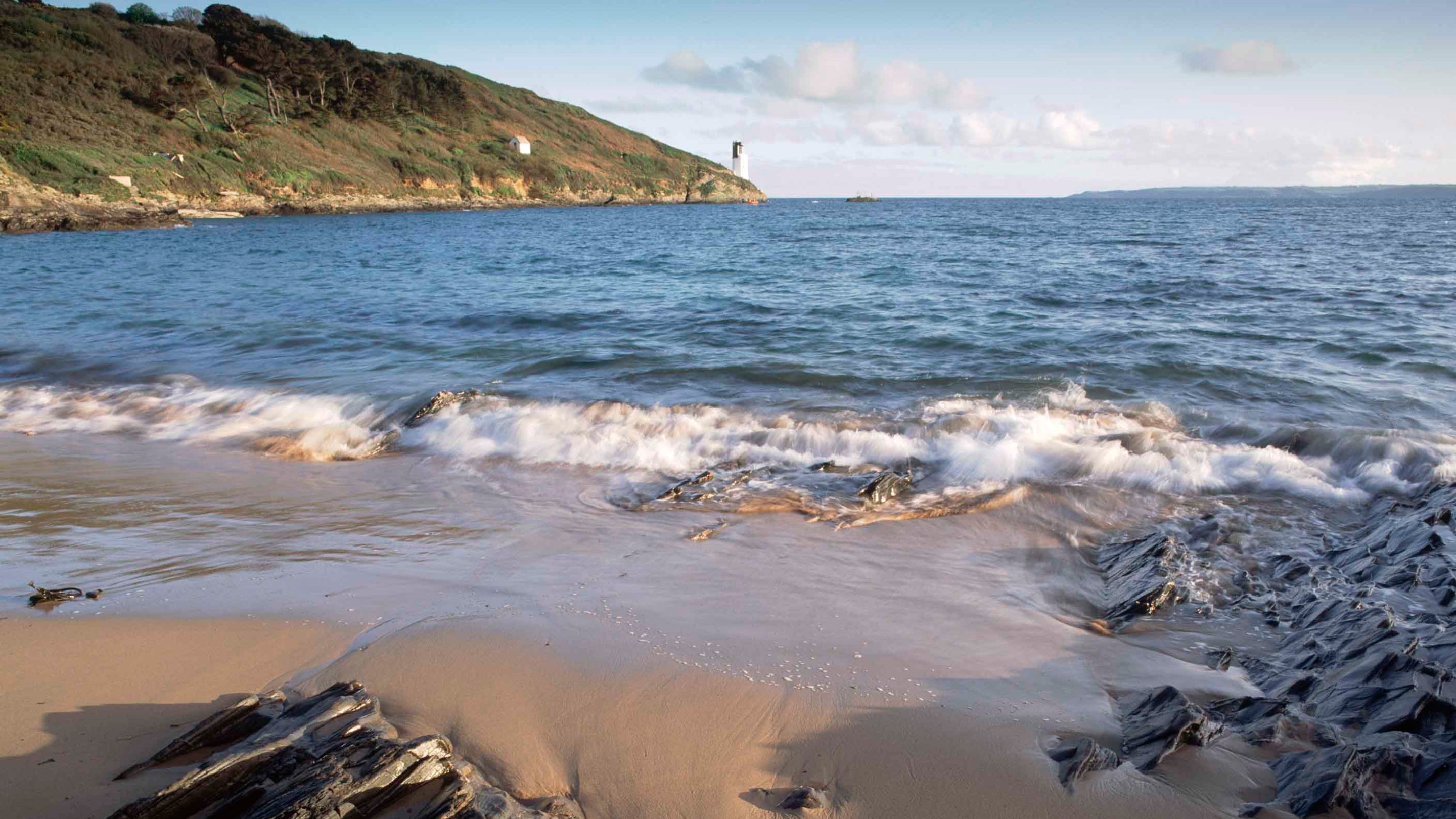 View from Great Molunan beach towards the lighthouse on St Anthony Head, near Falmouth, Cornwall. The lighthouse can be seen near the water's edge on the coast to the left.