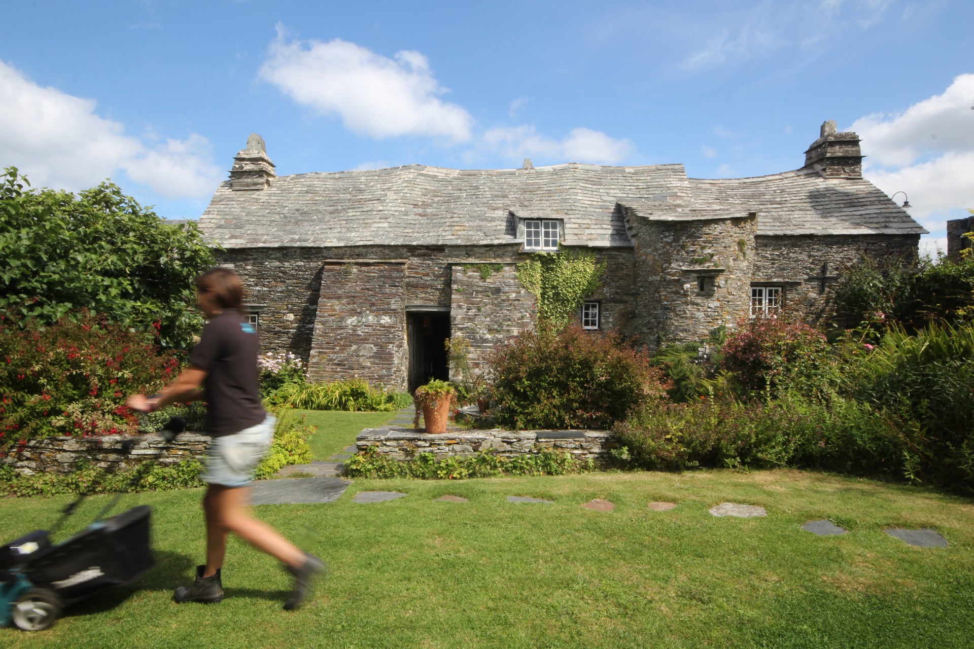 The gardener at Tintagel Old Post Office mowing the back lawn in the cottage garden