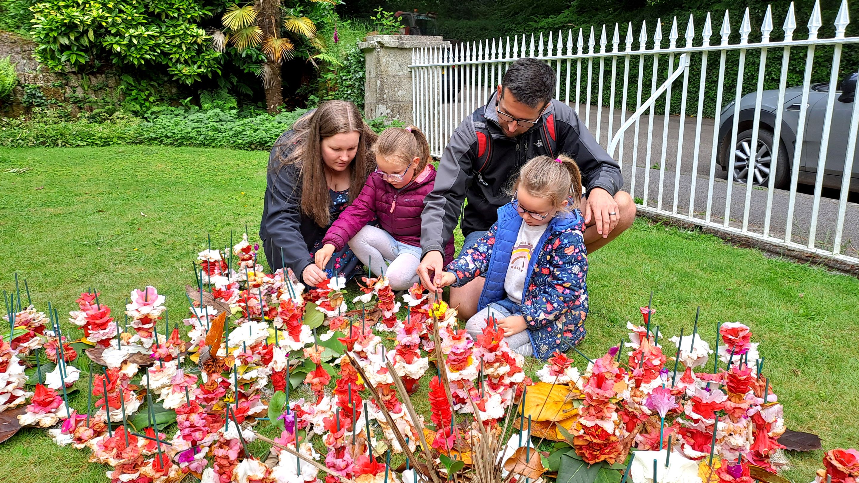 Two adults and two children on a lawn covered in fallen flowers on sticks