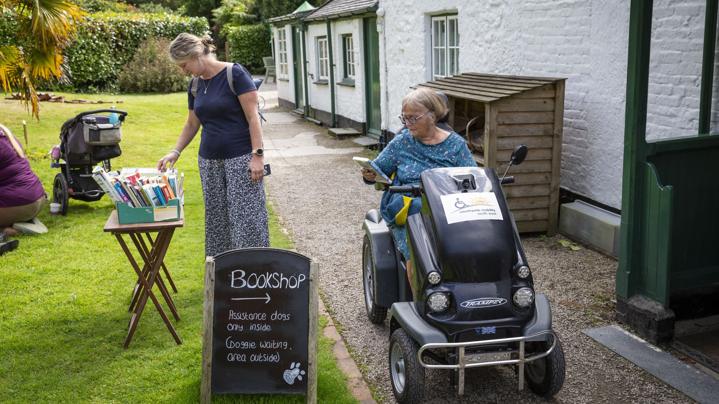 Woman using a mobility Tramper with a friend looking at books on a table outside a bookshop
