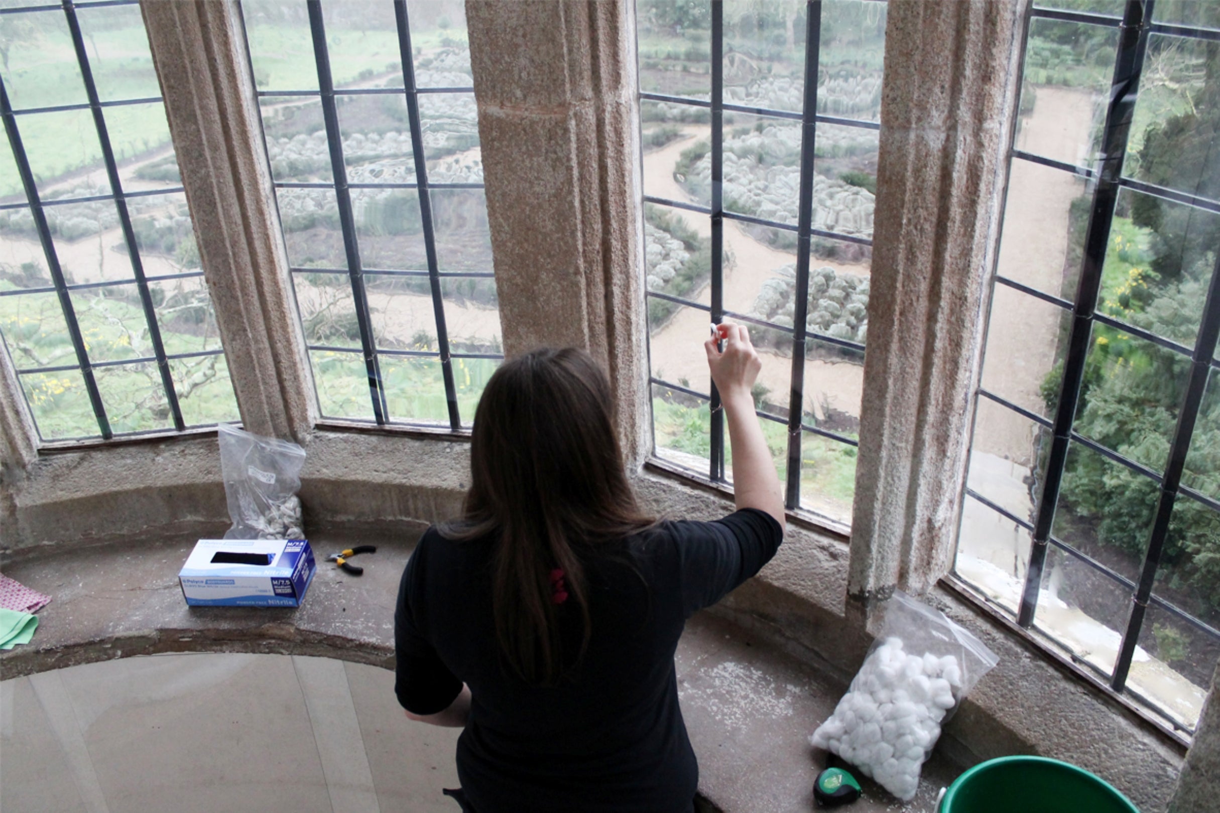A member of staff cleaning the solar window with the knot garden in the background, Trerice, Cornwall