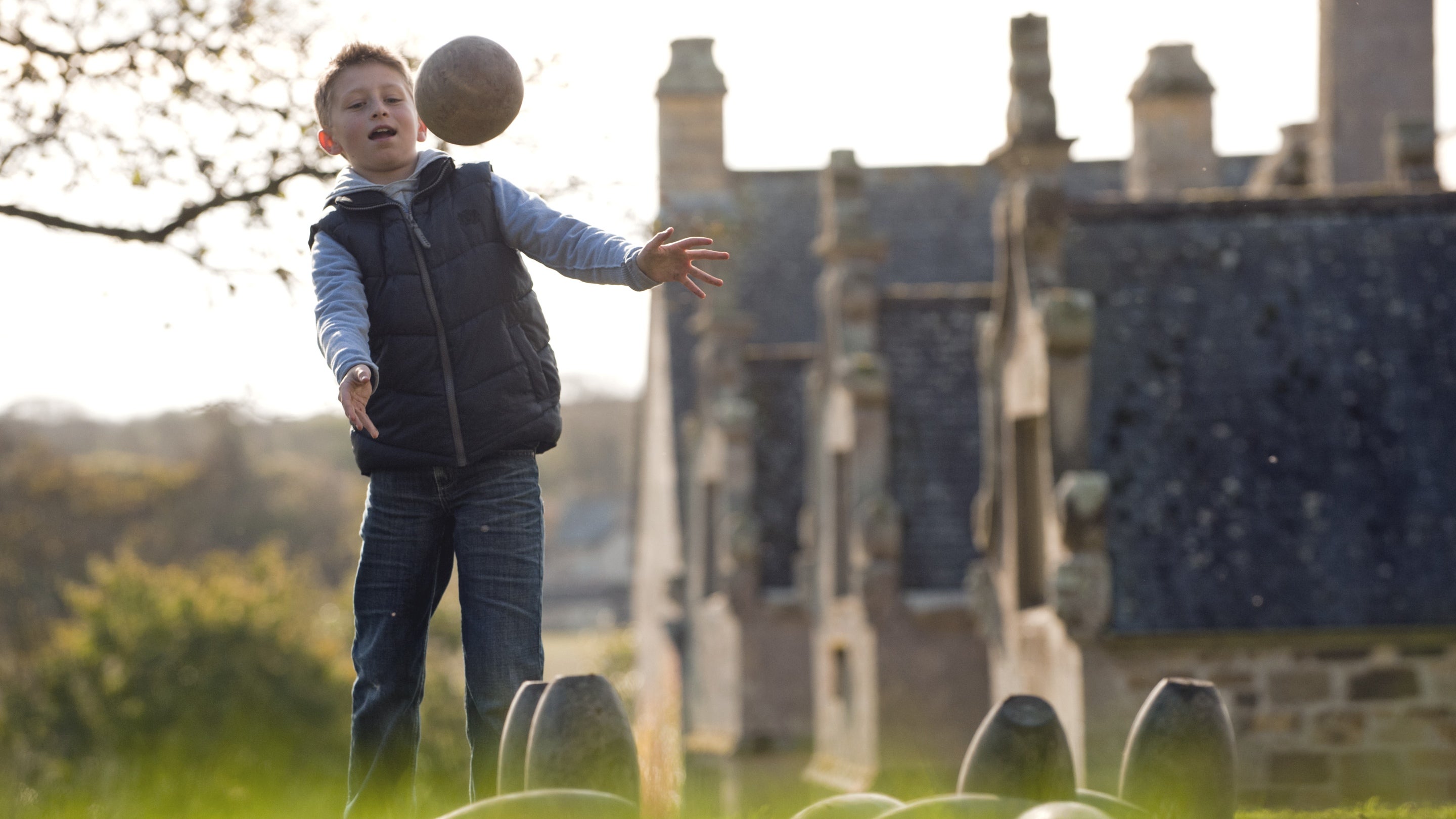 Child playing a traditional game of Kayling, a sort of garden skittles, at Trerice, Cornwall.