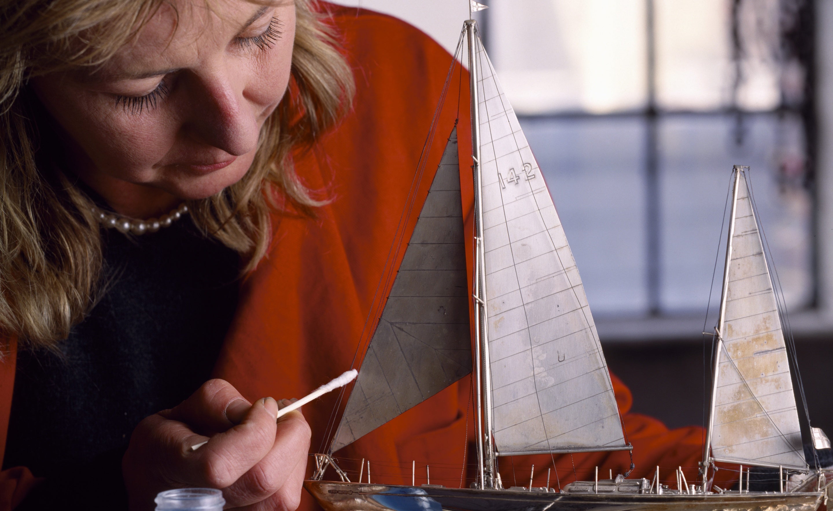 Deteriorated lacquer being removed from a silver boat, from Arlington Court. Sally Bowling uses a solvent on a cotton wool swab on a stick, whilst holding the boat with gloved hands.