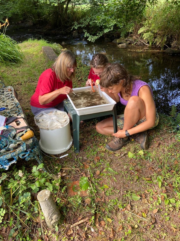 Three people gathered around a bucket with water in it