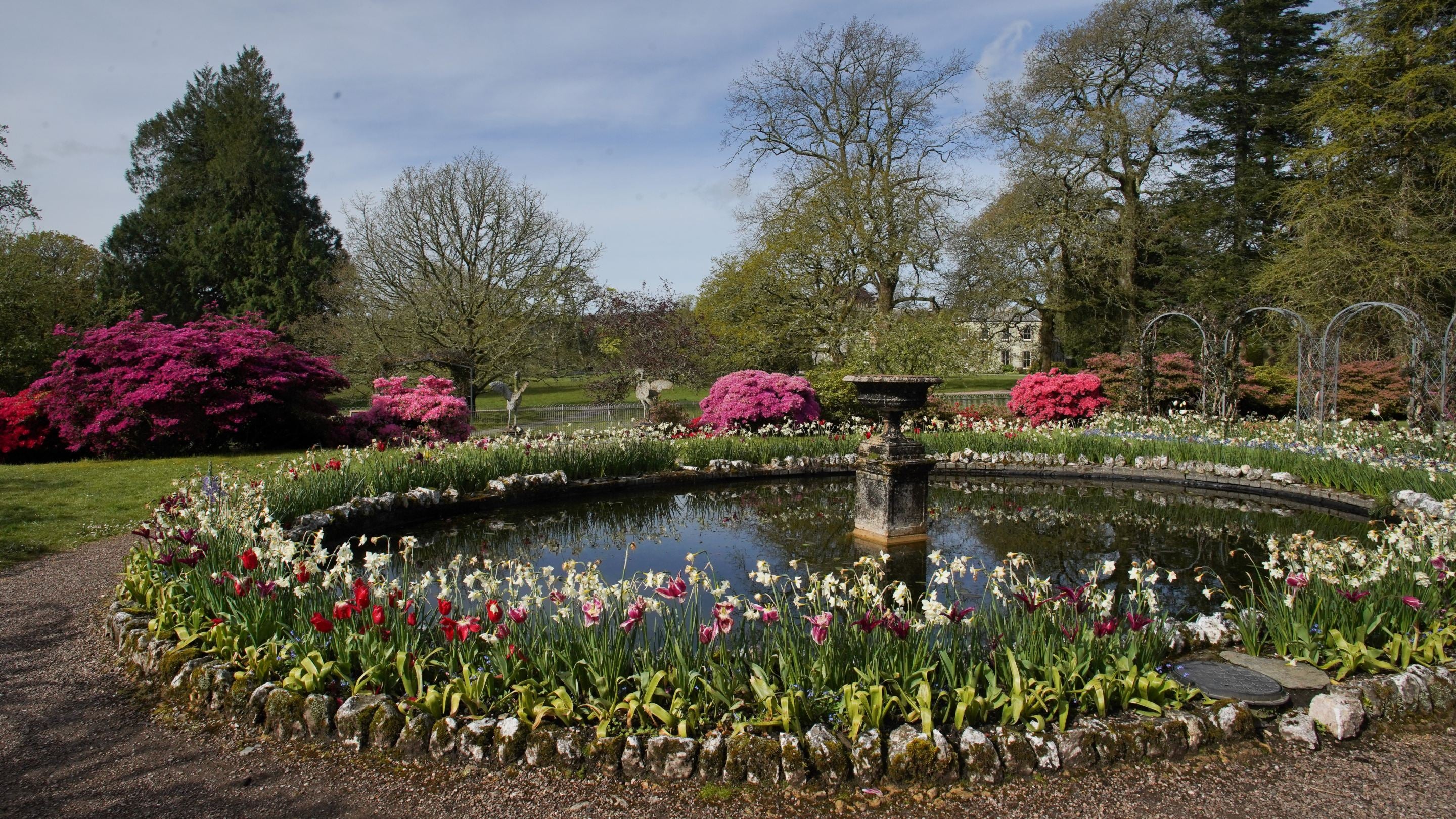 A pond with flowers surrounding the outside and a sundial in the middle