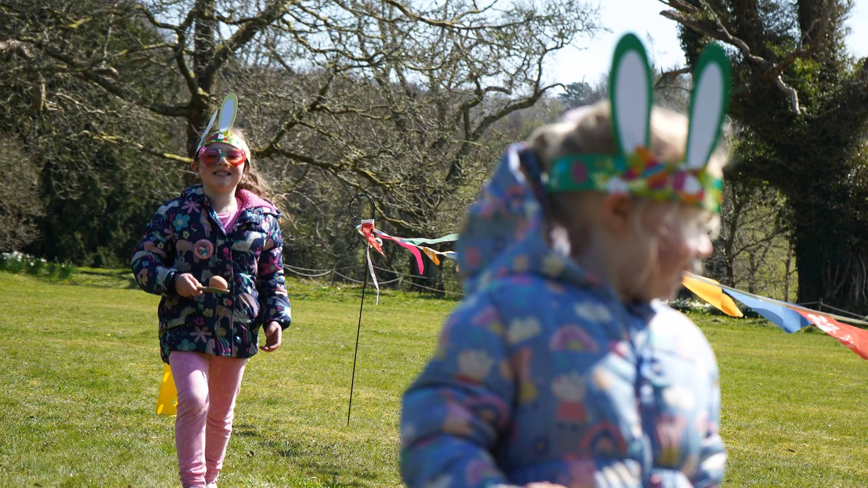 Two girls wearing bunny ears and balancing eggs on wooden spoons