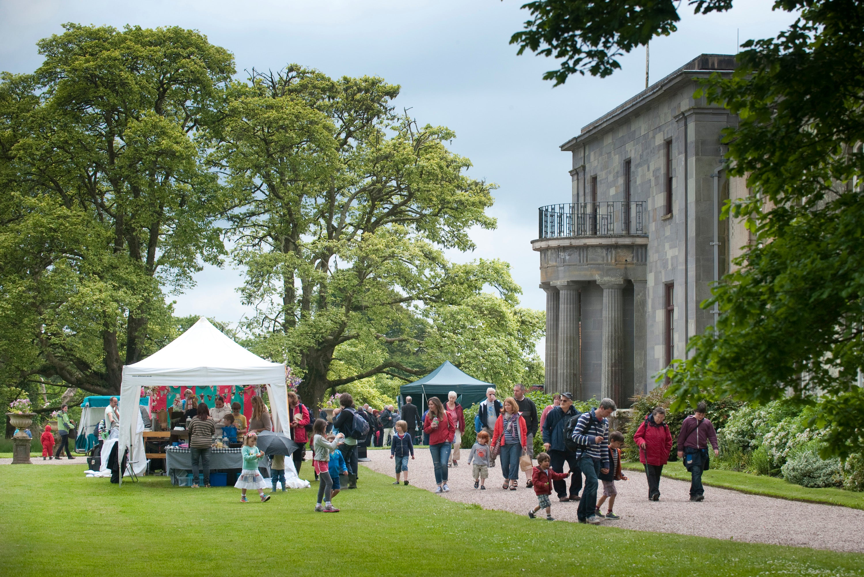 A fair on the lawn at Arlington Court, with smiling people and stalls set against the back drop of an impressive regency house.