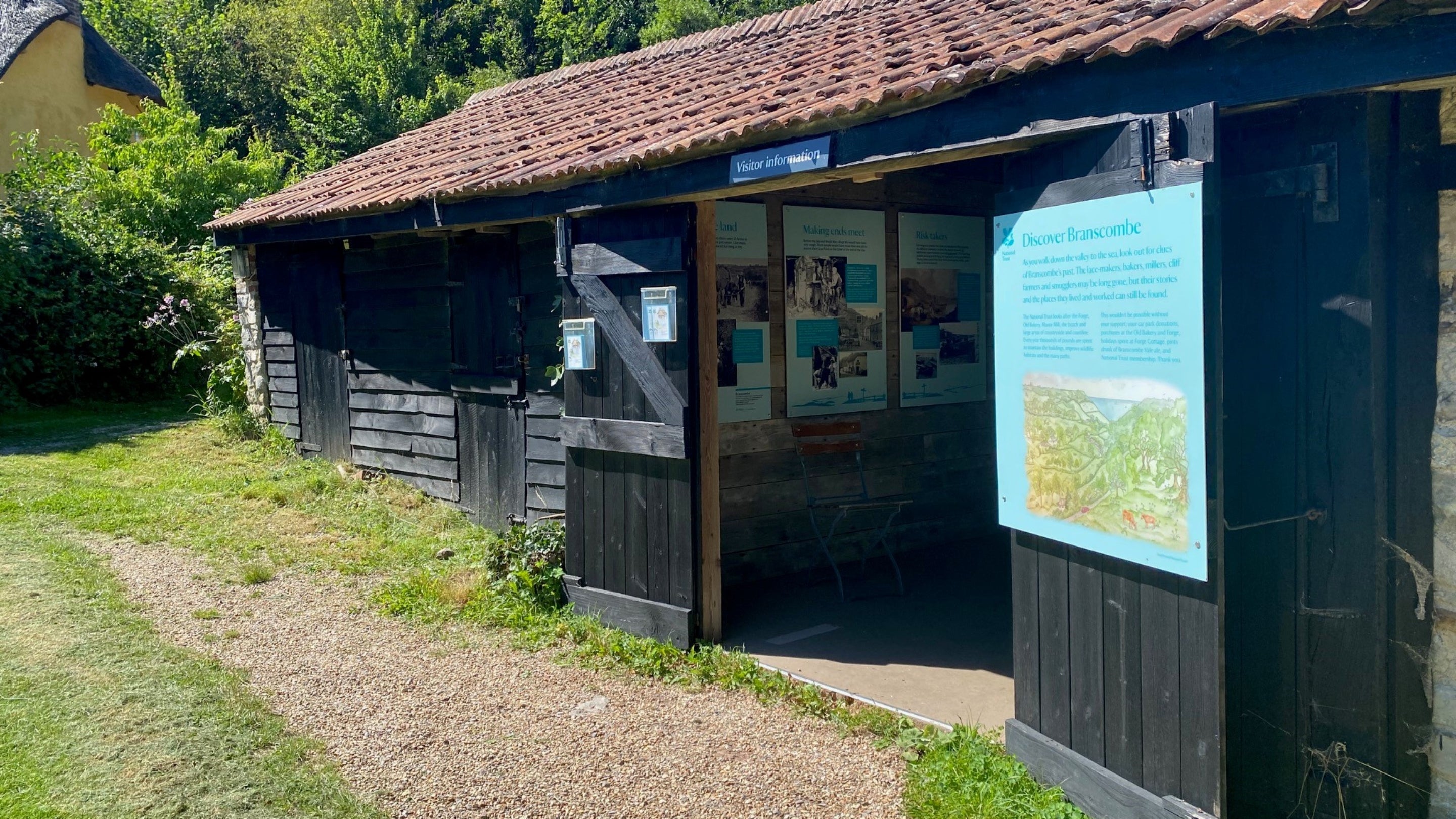 Gravel track leading to a door way to a stone building with visitor information boards on the walls