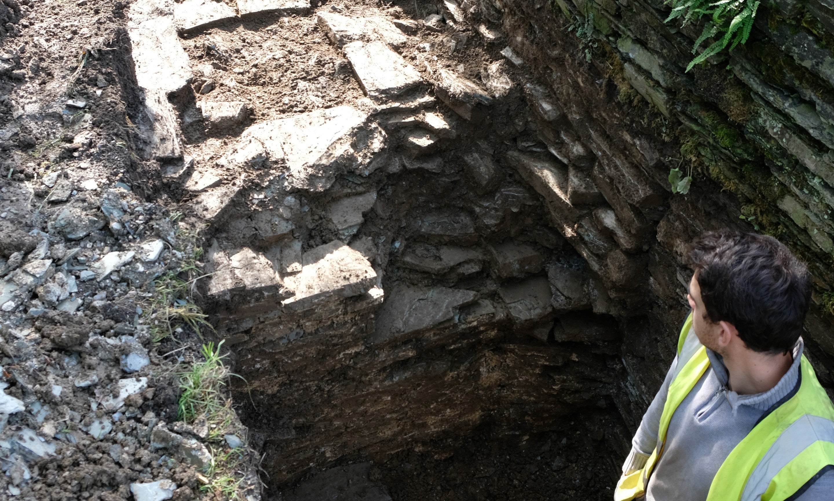 A man in a high-viz jacket assesses stone steps in a hole
