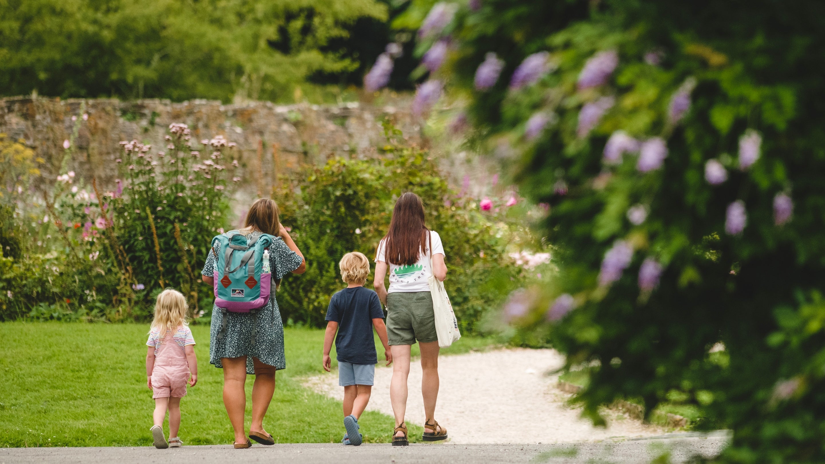 A family with two adults and two children walk towards the rose garden at Buckland Abbey.