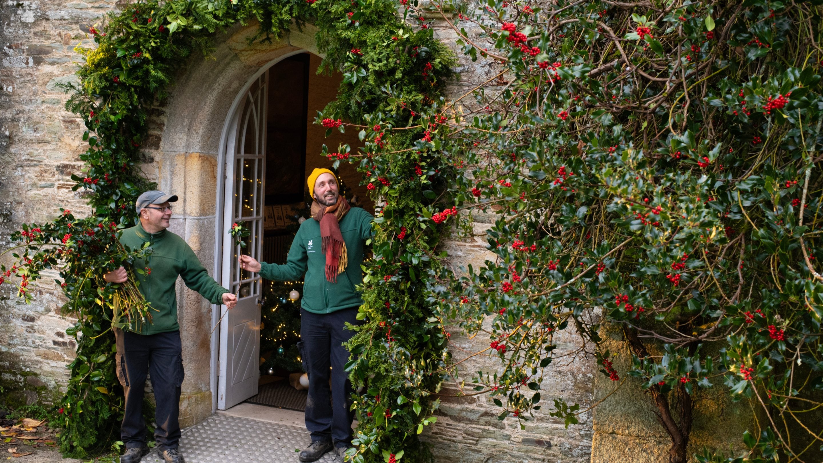 Volunteers and staff using holly to decorate the front door for Christmas at Buckland Abbey, Devon