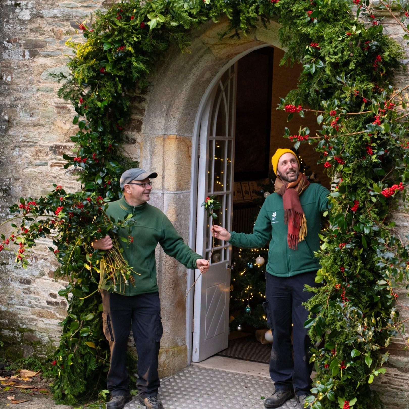 Volunteers and staff using fresh holly to decorate the front door for Christmas at Buckland Abbey, Devon