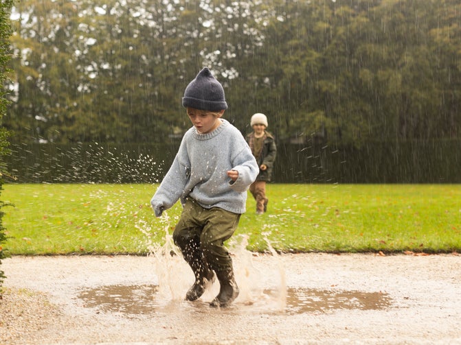 Boy jumping in a puddle. The boy is wearing a woolly hat and wellies