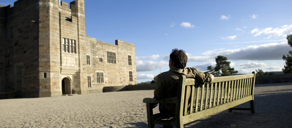 Visitor sitting on a bench looking at the sun on the entrance tower at Castle Drogo, Devon.