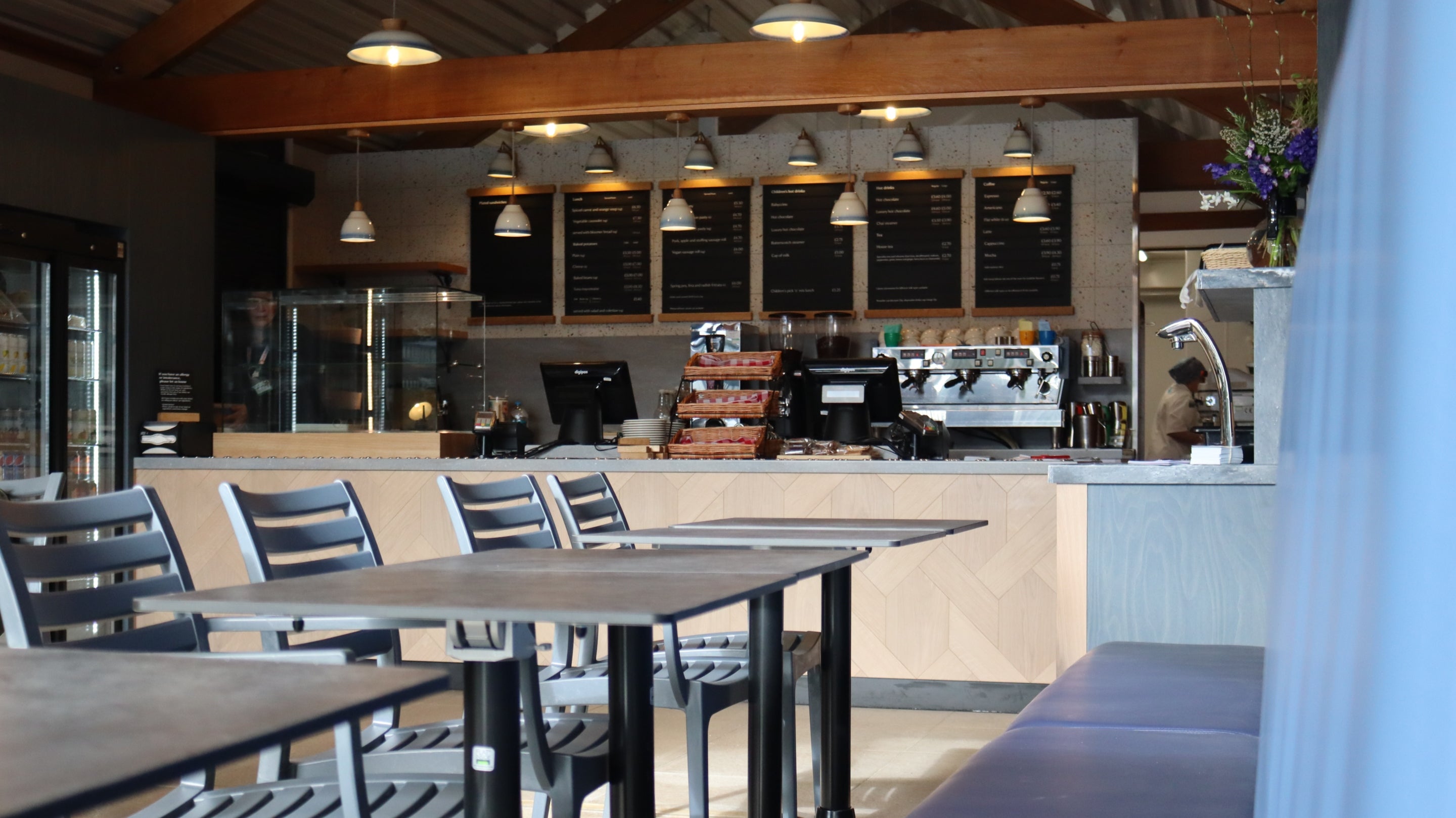 View of the cafe with booth seating to the right, grey square chairs to the front and a counter at the back.