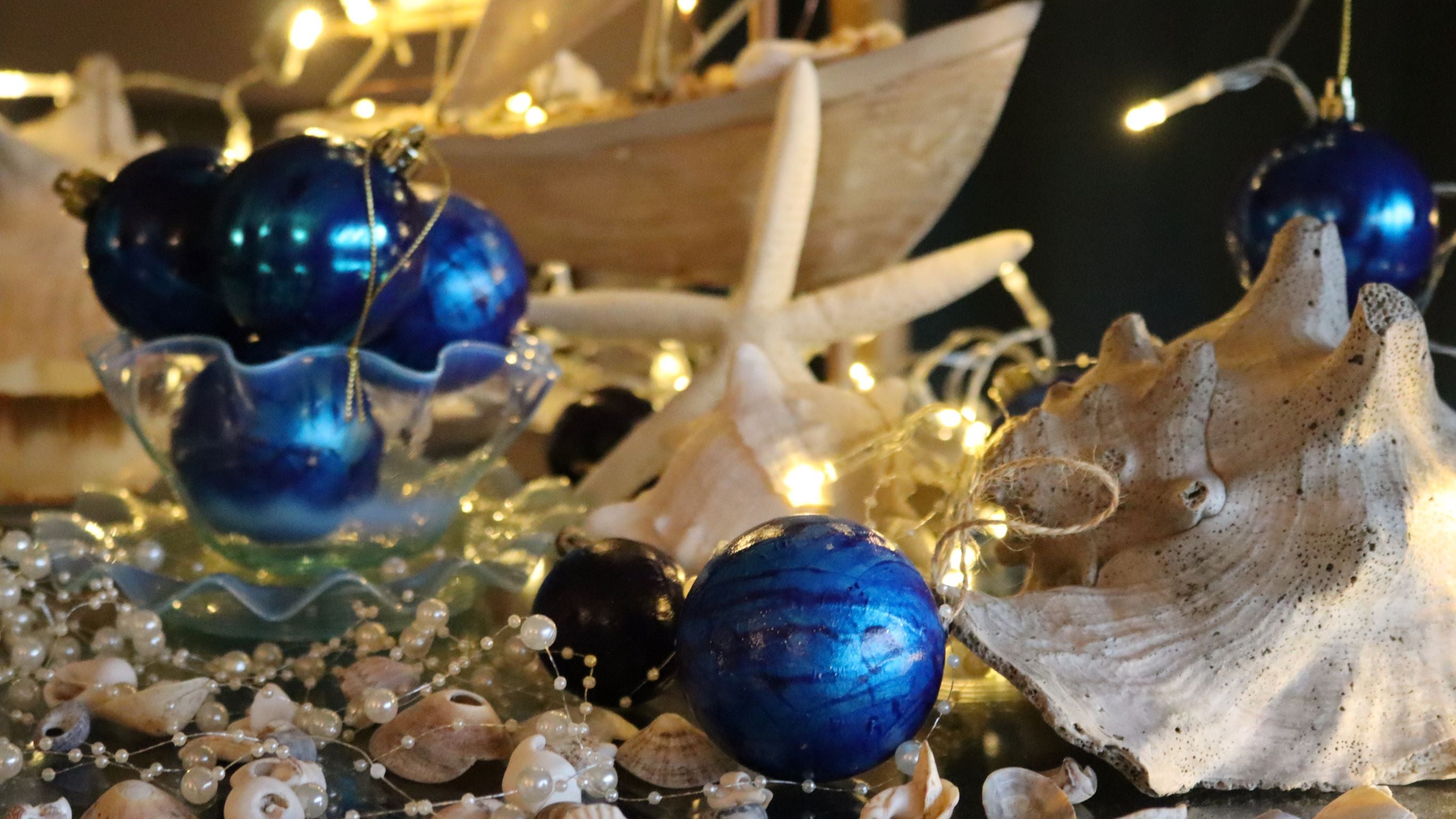 Blue baubles scattered on a table with white shells and starfish, and blurred fairylights in the background.